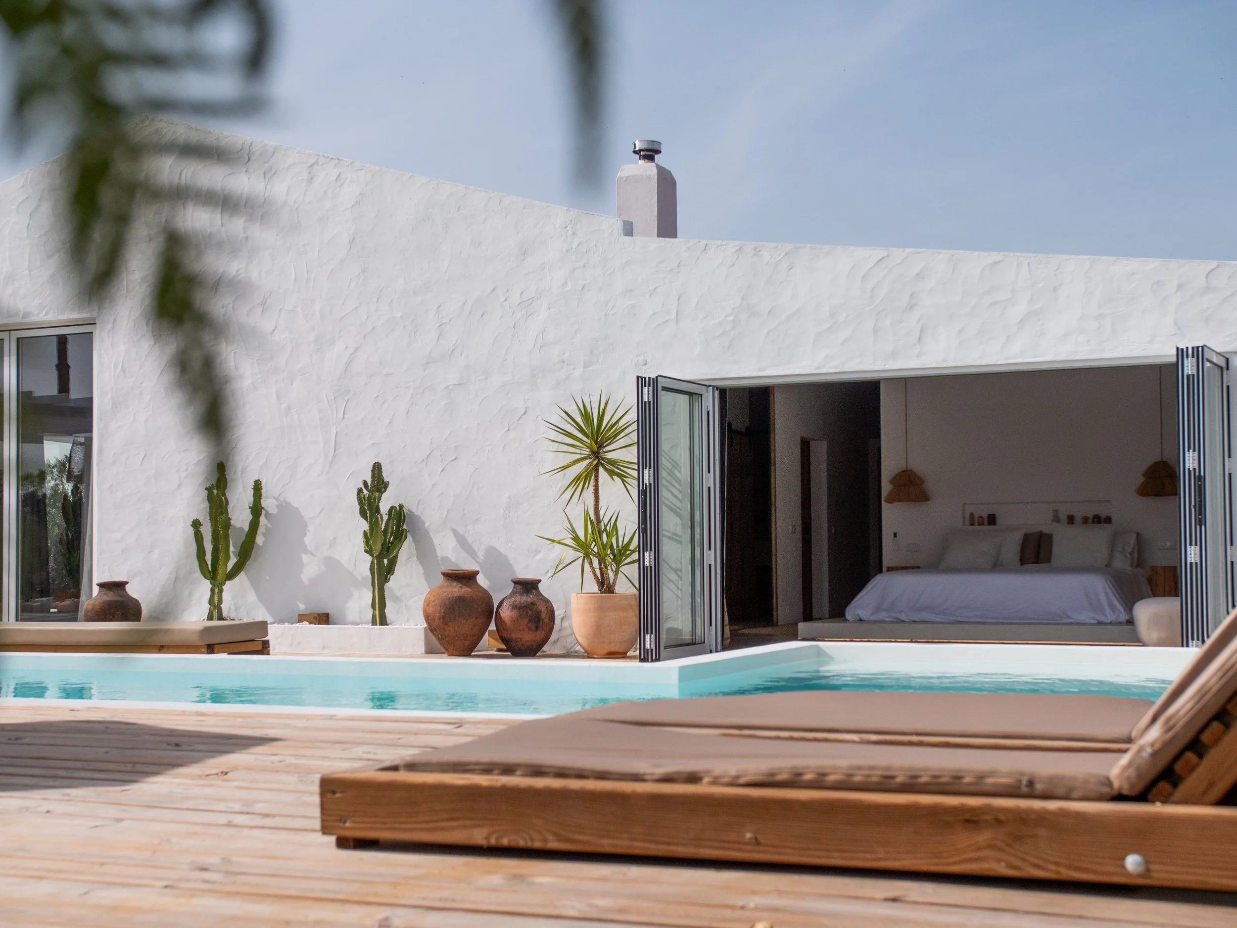 The pool, lounge chairs and open bedroom doors at Casa Thala on a clear day.