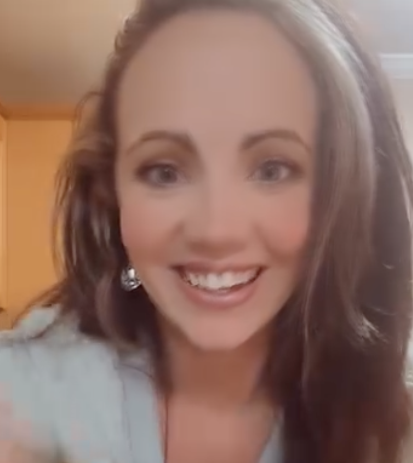 Close-up of a smiling woman with shoulder-length brown hair and earrings, indoors.