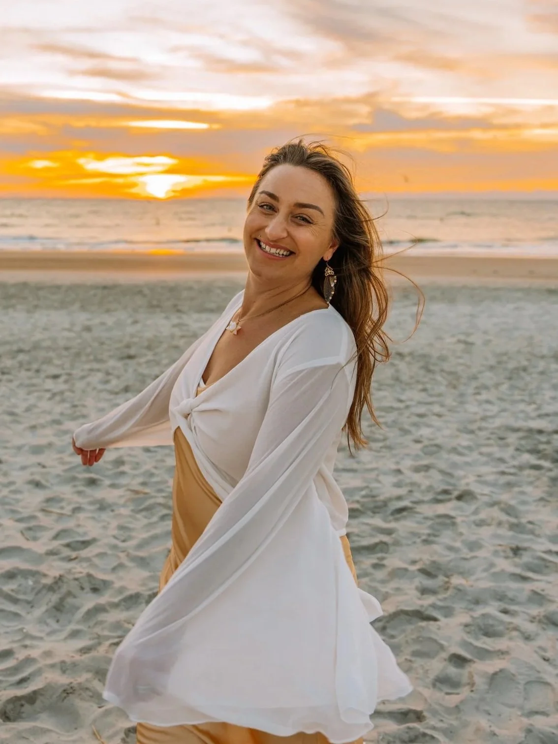 Smiling woman in white and beige dress on beach at sunset