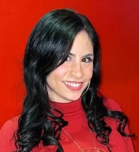 Woman with long black hair wearing a red top smiling against an orange background.