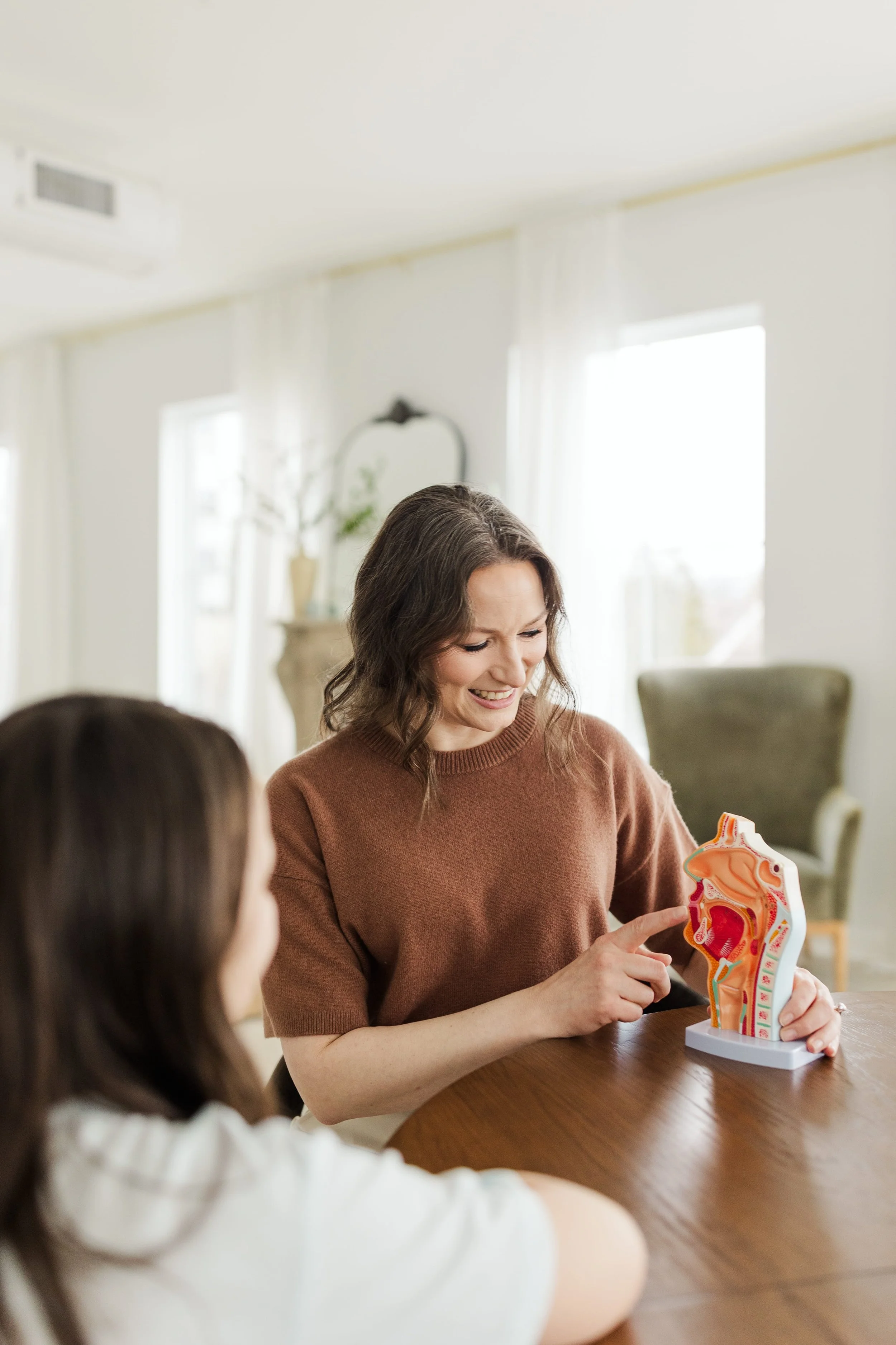 Adult woman and girl examining a model of the human digestive system at a table in a bright room.