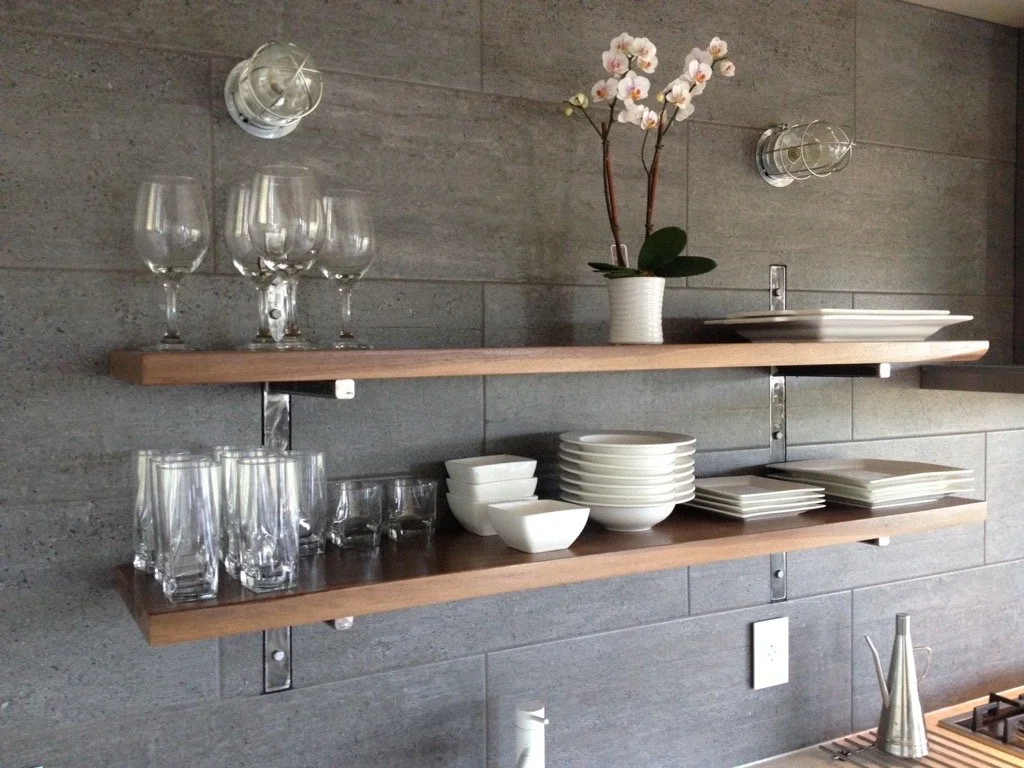 Two wooden shelves on a gray wall holding glassware, dishes, and a potted orchid plant.