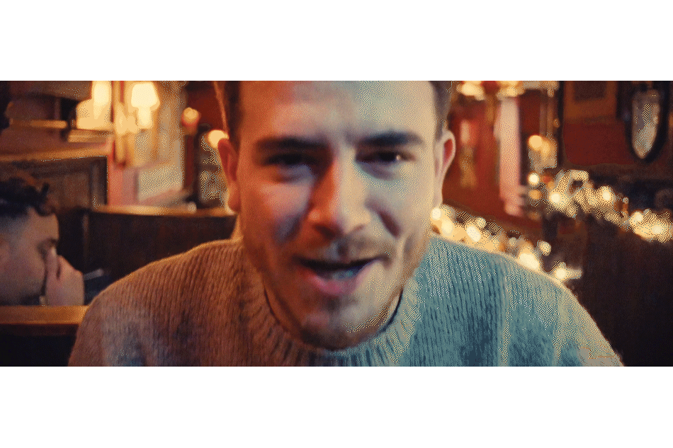 Close-up of a young man smiling and talking in a warmly lit restaurant or bar with festive decorations.