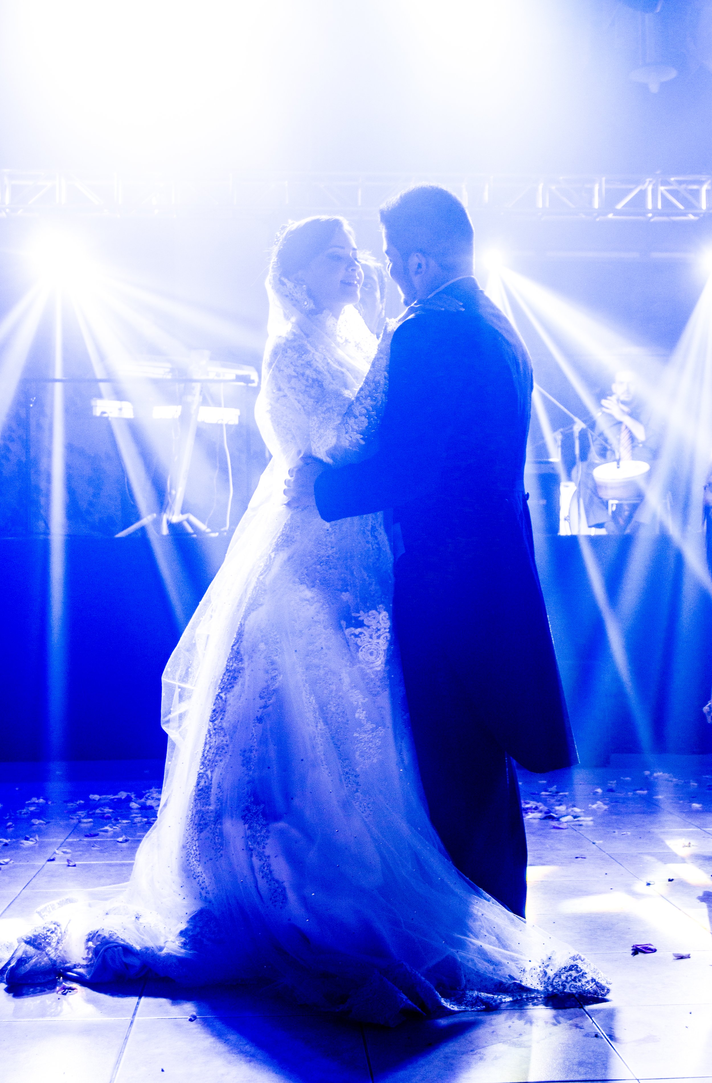 A bride and groom dance together at their wedding reception with bright stage lights in the background.