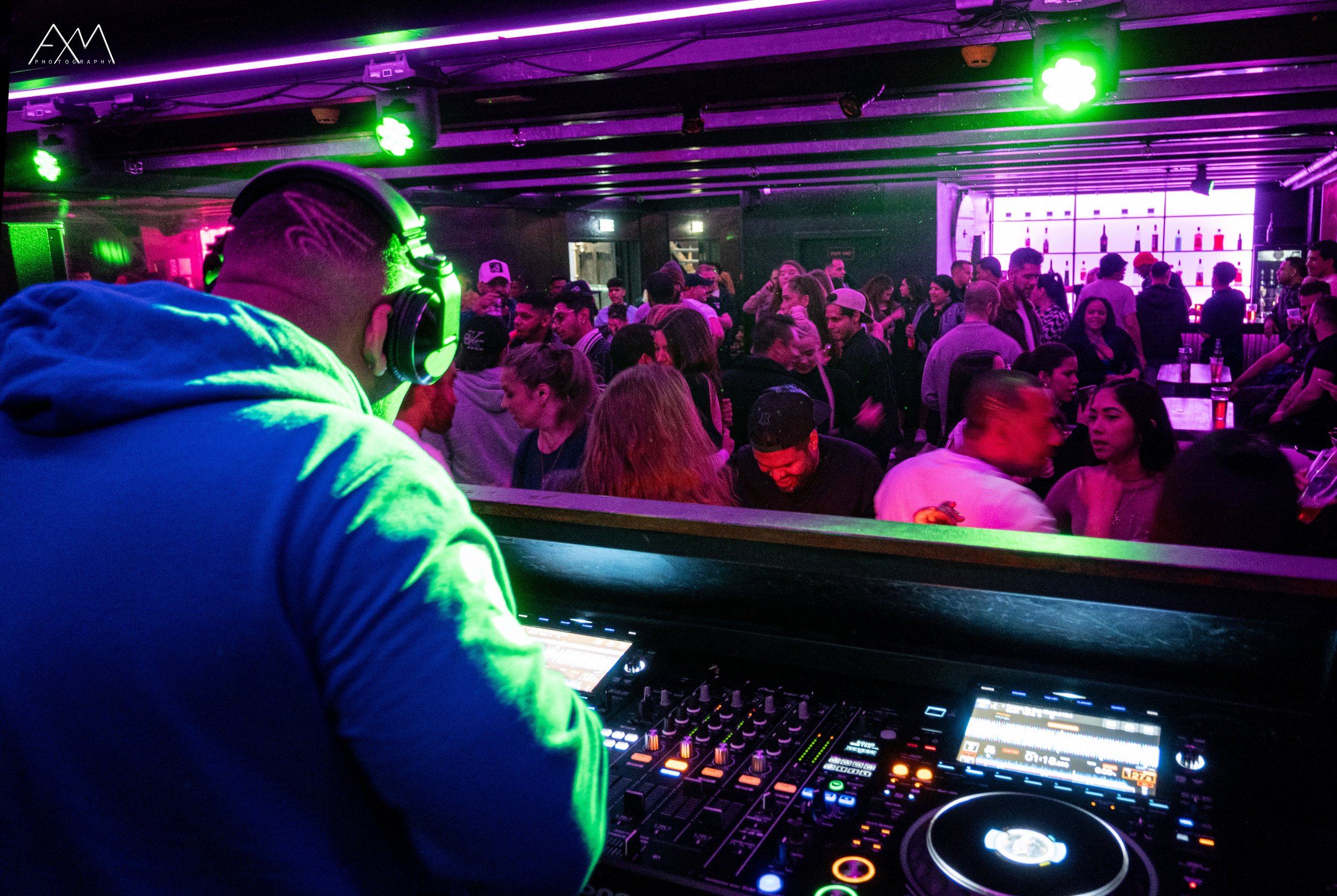 DJ performing at a crowded nightclub with colorful lighting and many people dancing and socializing.