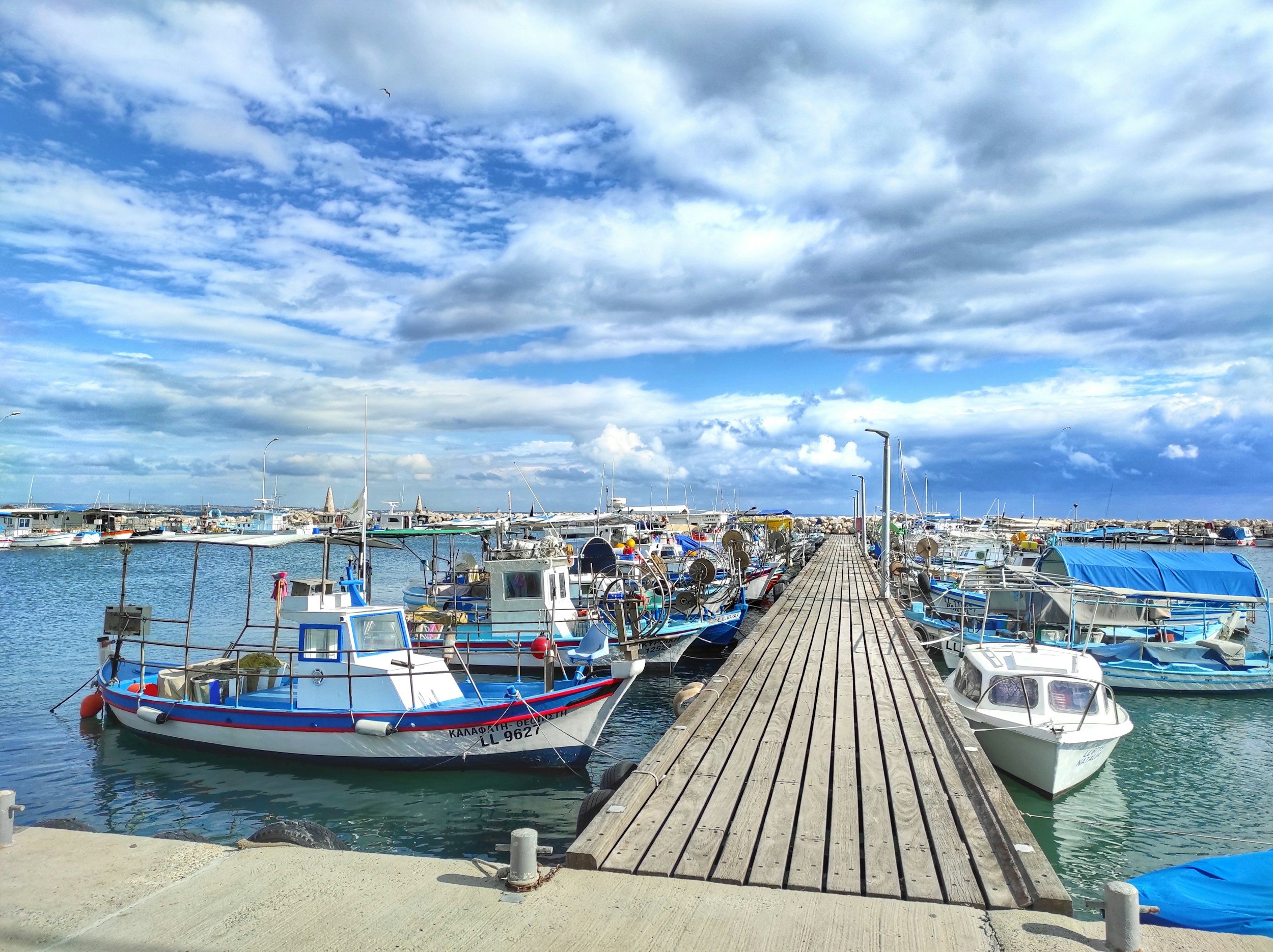 A marina with numerous boats docked along a wooden pier under a partly cloudy sky.
