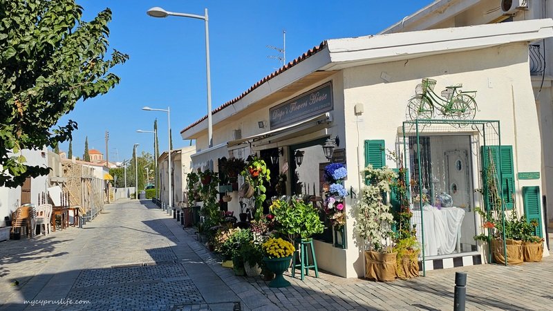 A small shop on a quiet cobblestone street, decorated with colorful flowers and a green bicycle sculpture on the wall.