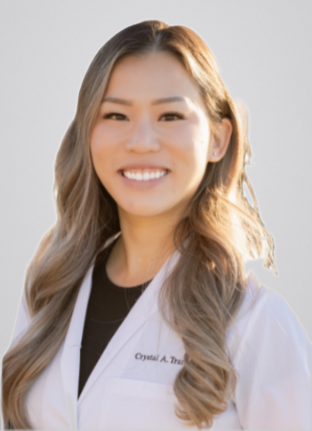 A woman with long wavy hair wearing a white coat, smiling outdoors.