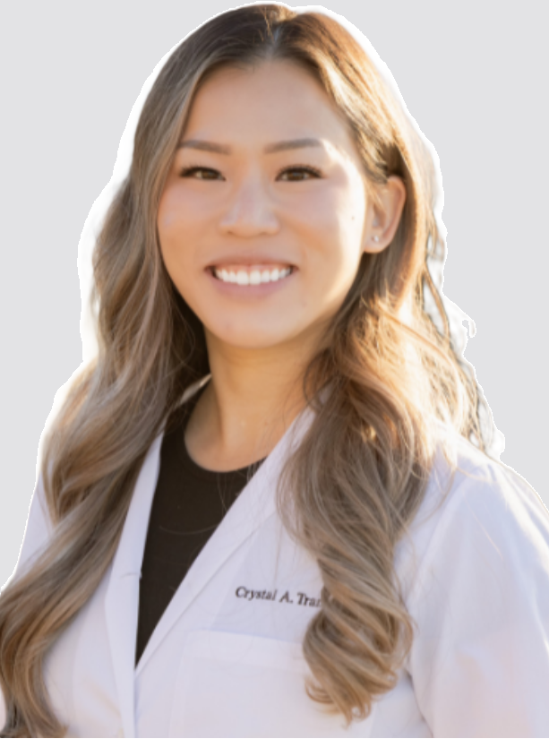 A woman with long wavy hair wearing a white coat, smiling outdoors.