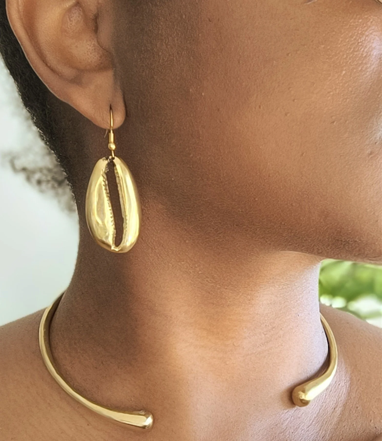 Une femme portant des bijoux en laiton, comprenant une boucle d'oreille en forme de coquillage et un collier de style col ouvert