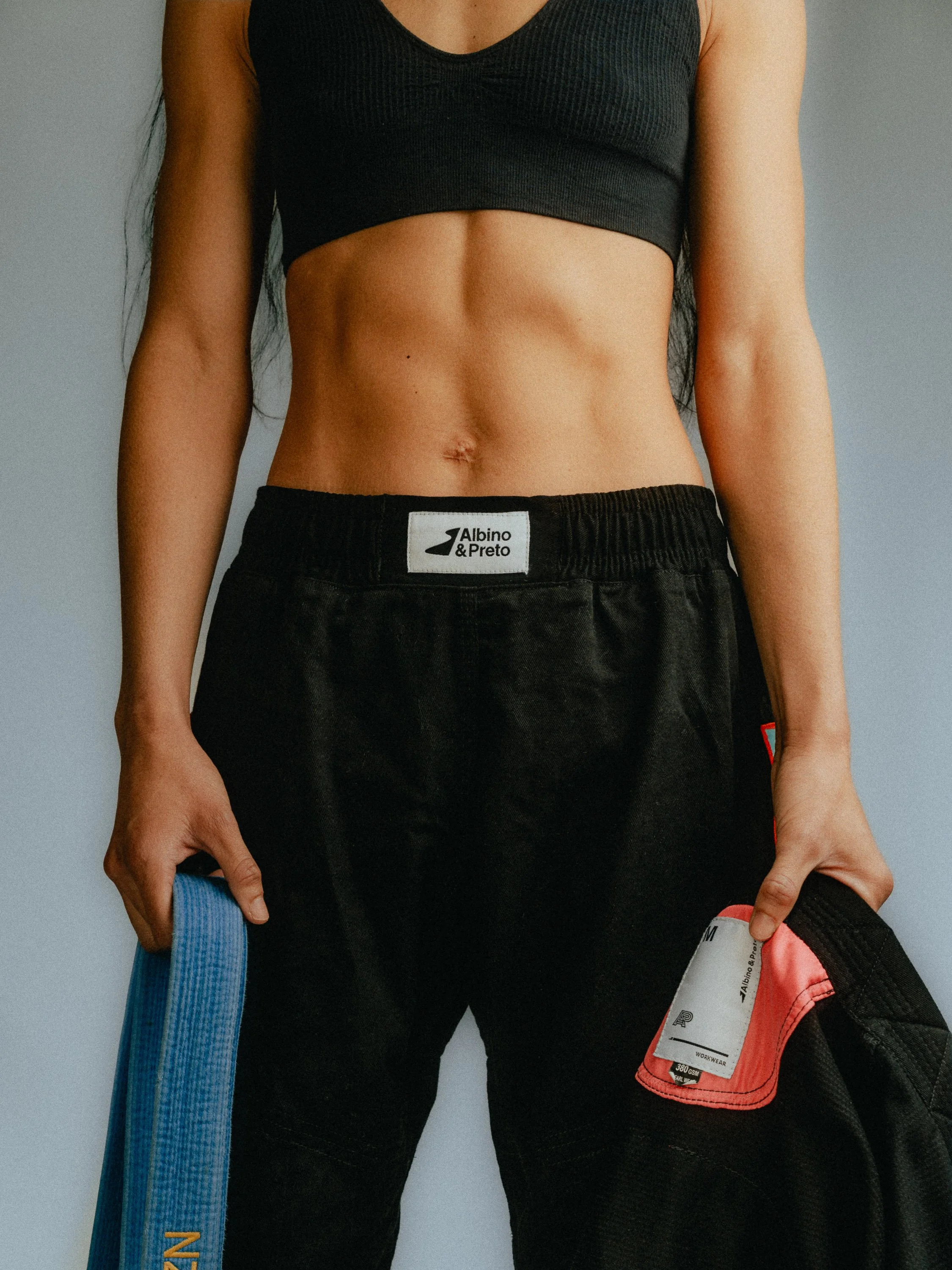 Close-up of a woman's midsection, wearing black sportswear, holding a blue and an orange belt. Personal Branding Photography and Headshots in London.