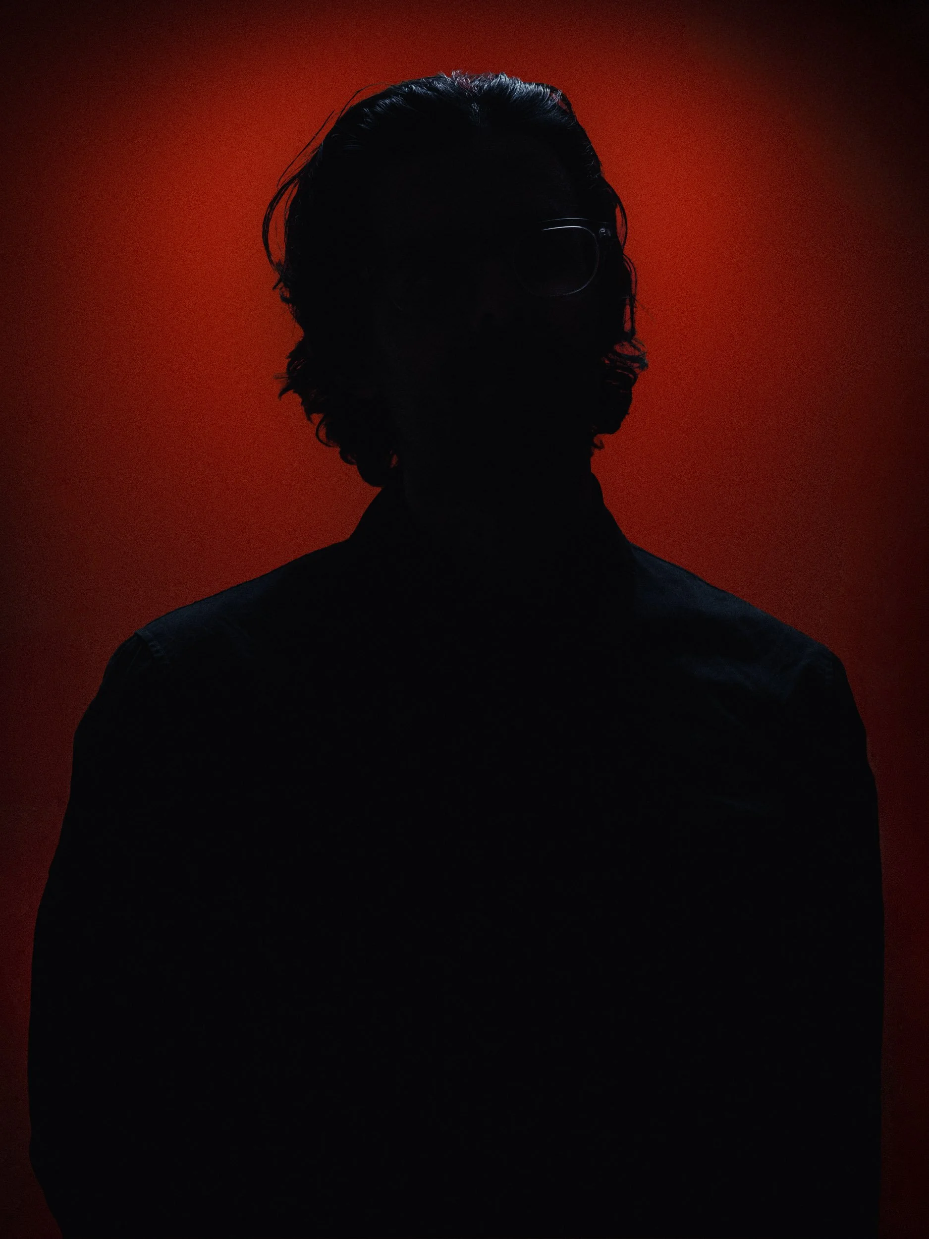 Silhouette of a person with dark hair and glasses against a red background. Personal Branding Photography and Headshots in London.