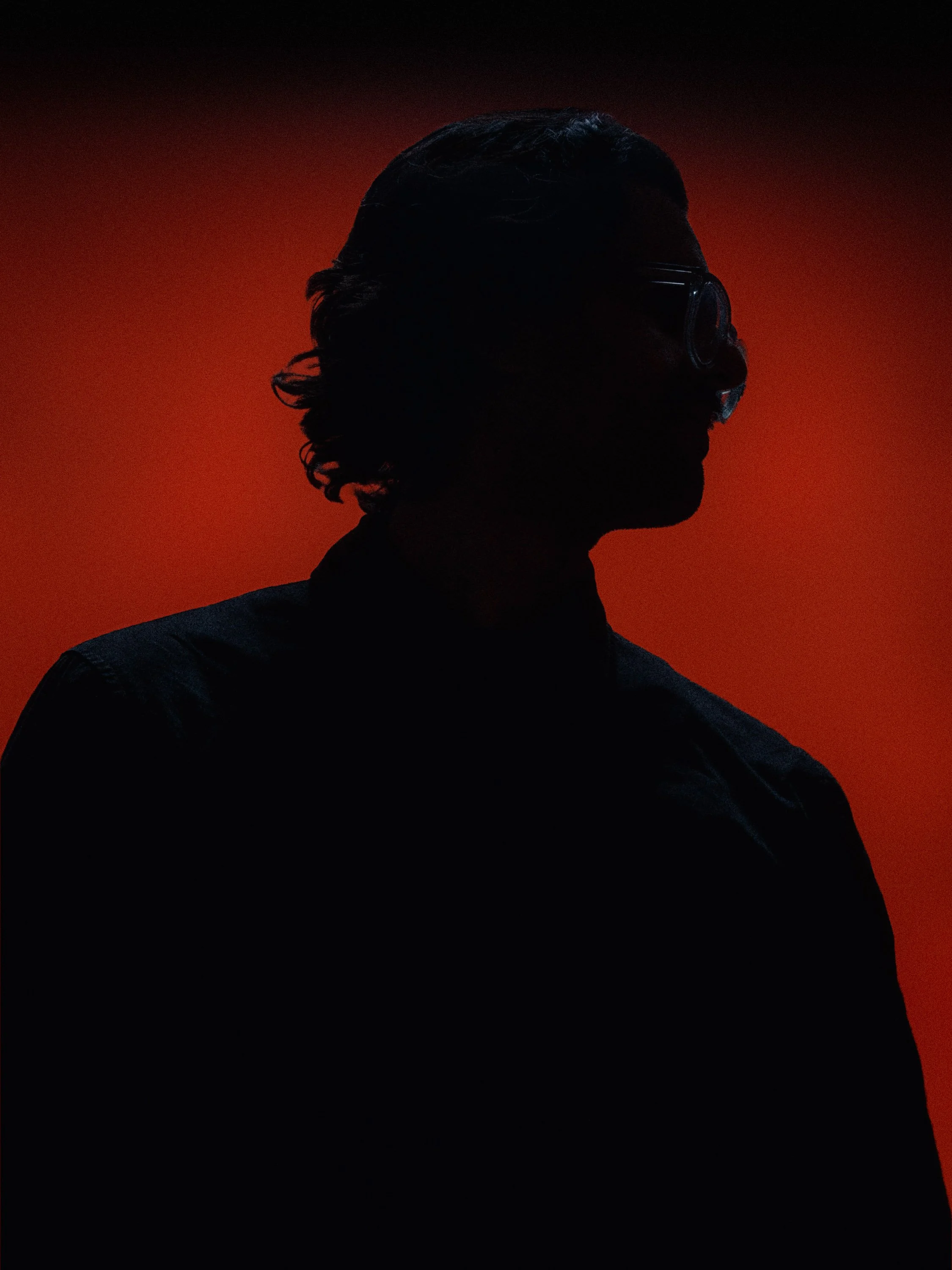 Silhouette of a man with wavy hair and glasses against a red background. Personal Branding Photography and Headshots in London.