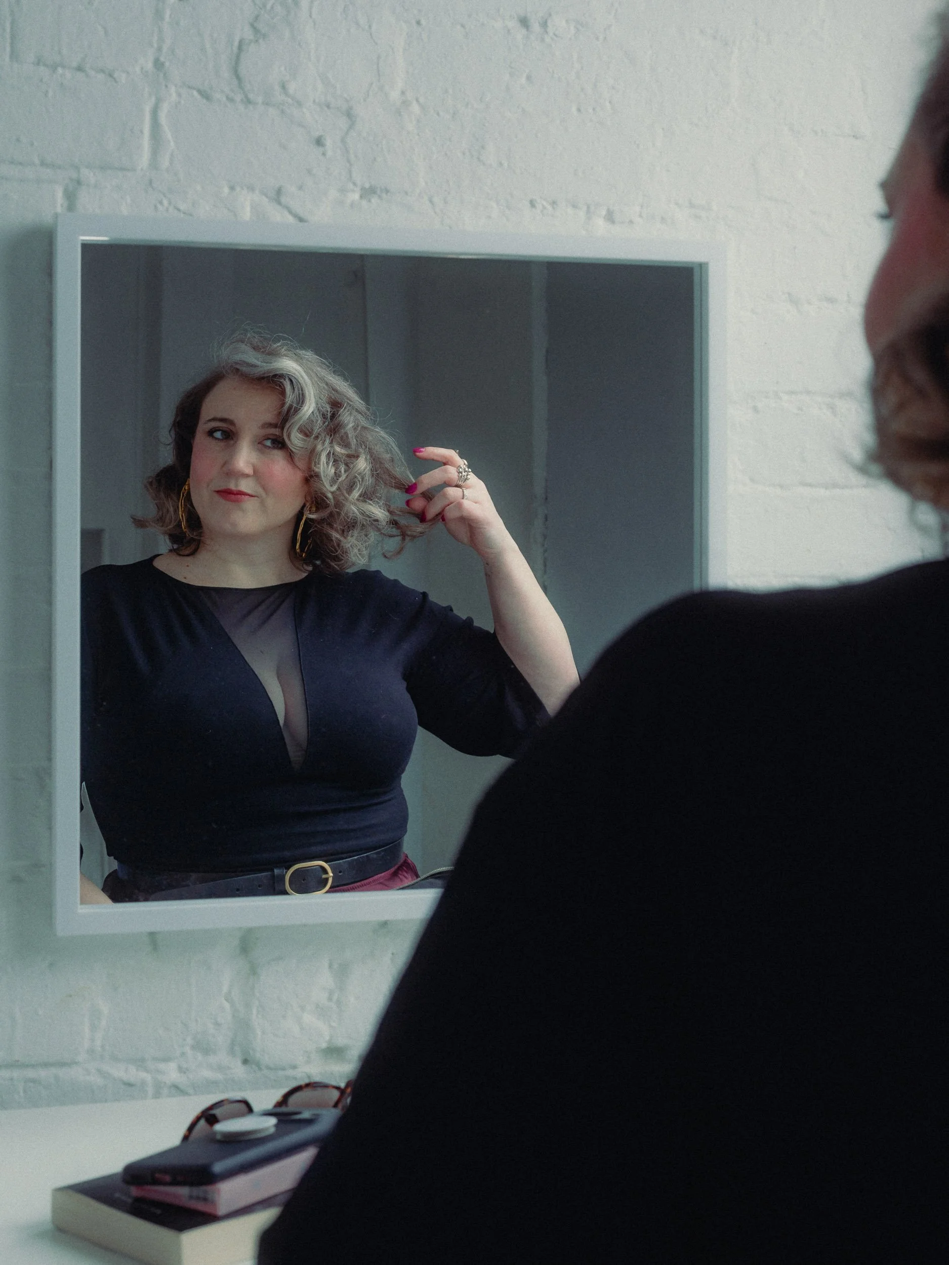 A woman gazing at herself in the mirror while fixing her hair. Personal Branding Photography and Headshots in London.