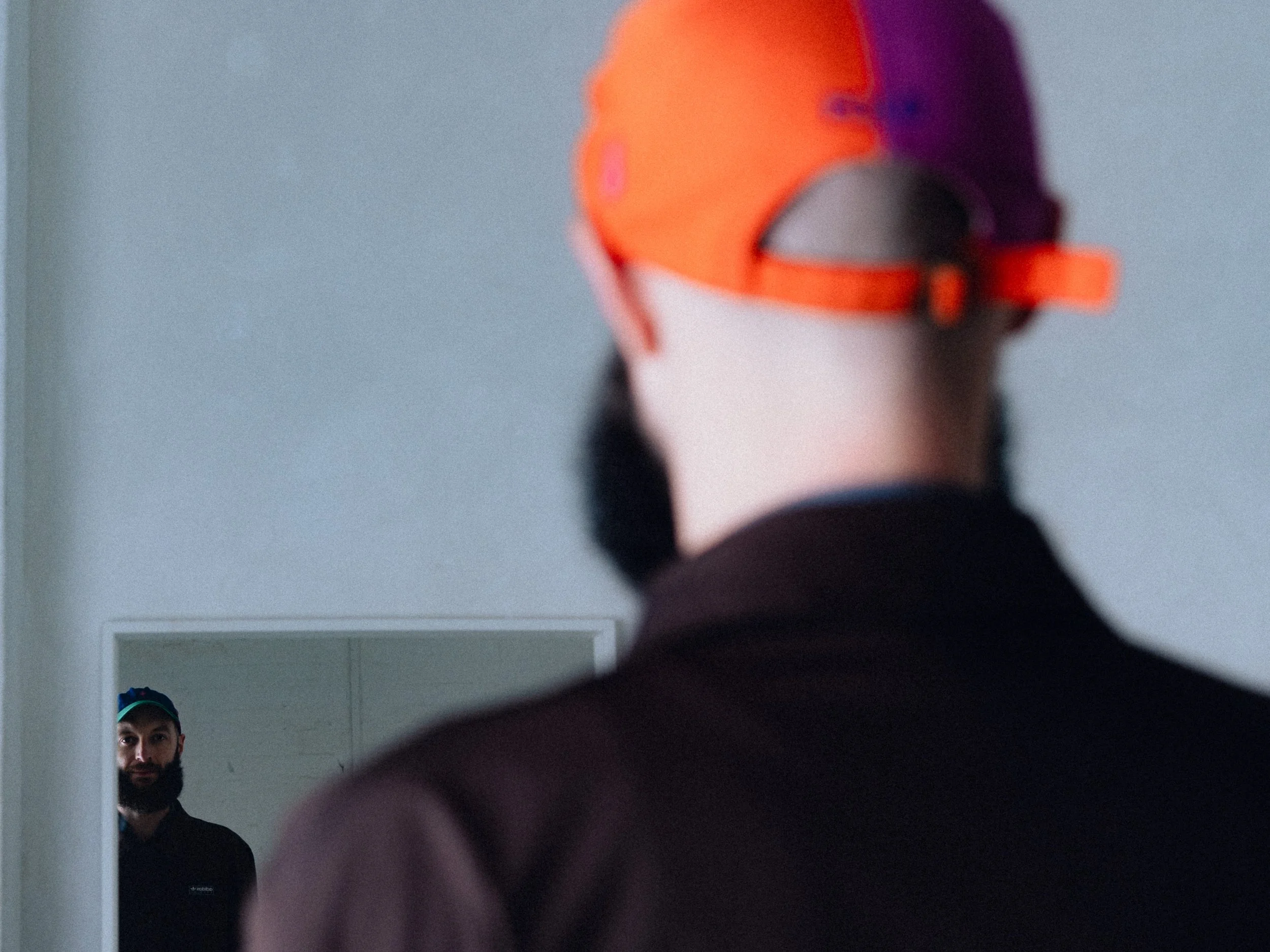 A man taking a selfie in the mirror, with the reflection showing his face, dark beard, and wearing a cap, while he faces away from the camera. Personal Branding Photography and Headshots in London.