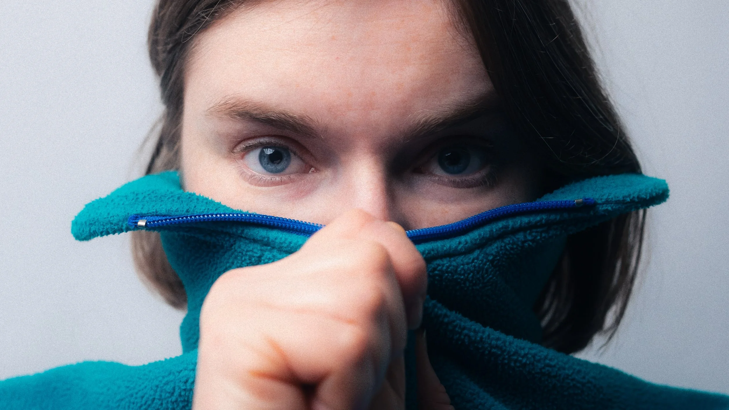 Close-up of a person with blue eyes, holding a blue fleece jacket up to their face. Personal Branding Photography and Headshots in London.