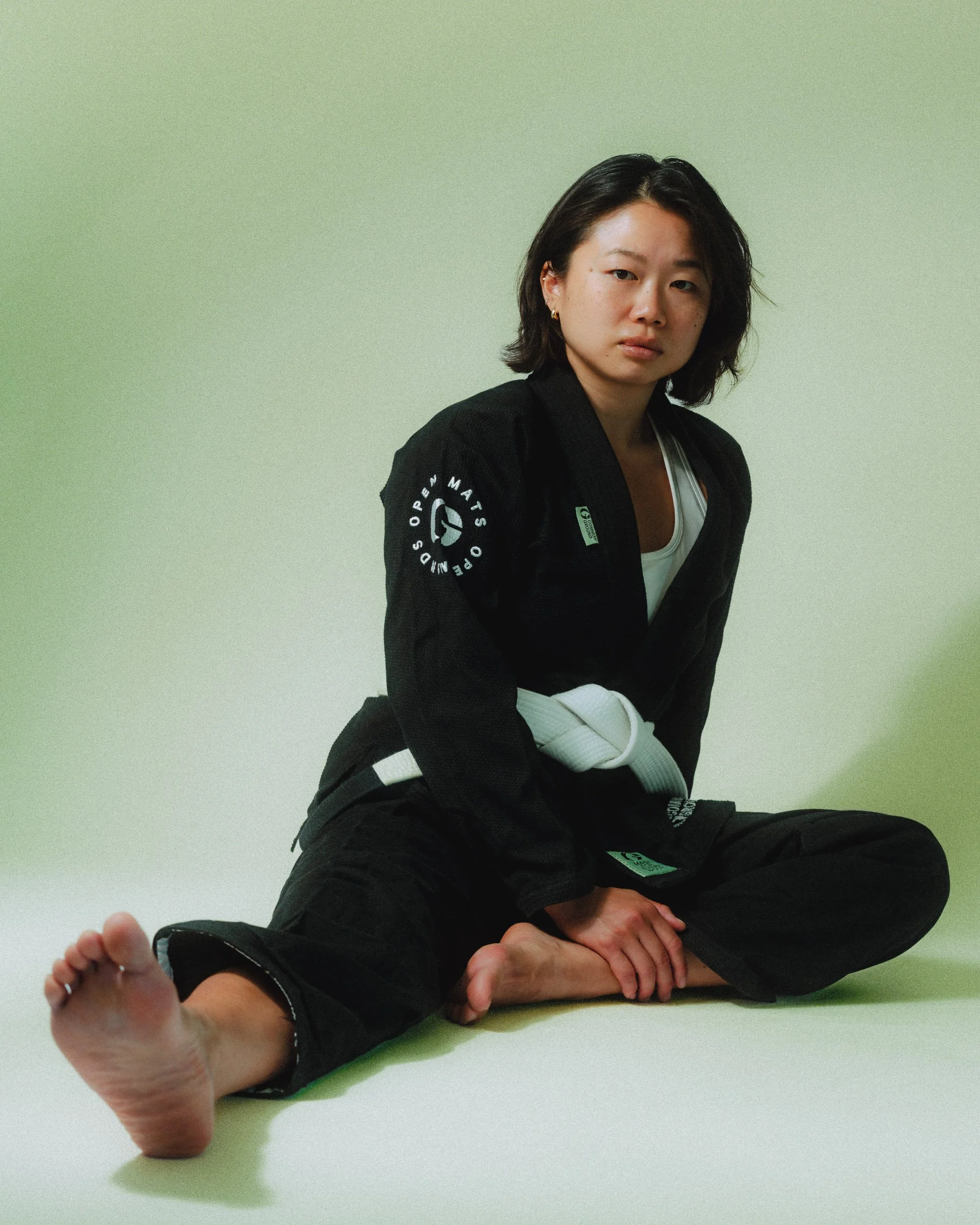 Young woman sitting on the floor in a martial arts uniform, with a white belt, against a plain light green background. Personal Branding Photography and Headshots in London.