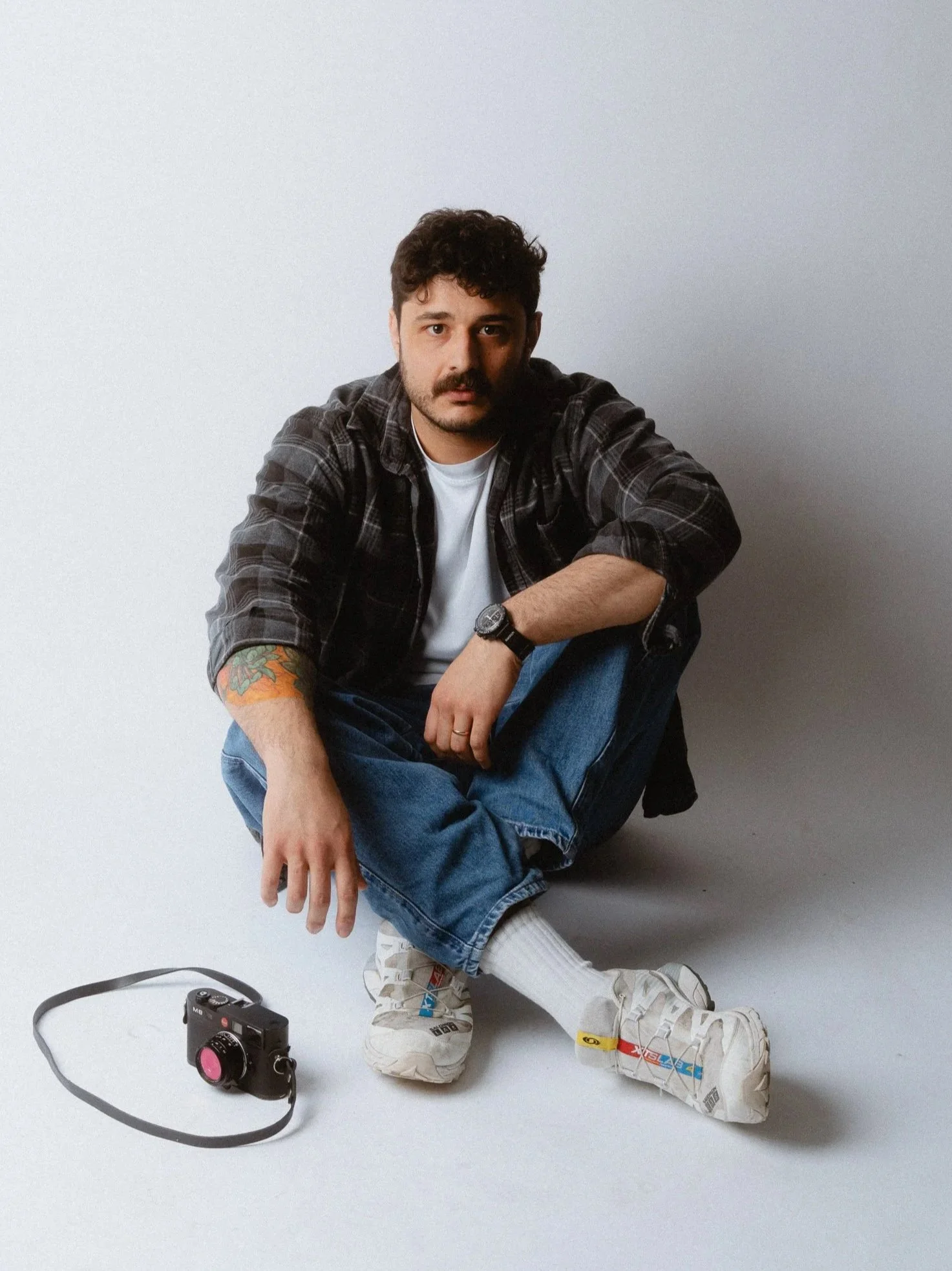 A man sitting on the floor with a camera on the ground in front of him. Personal Branding Photography and Headshots based in London.