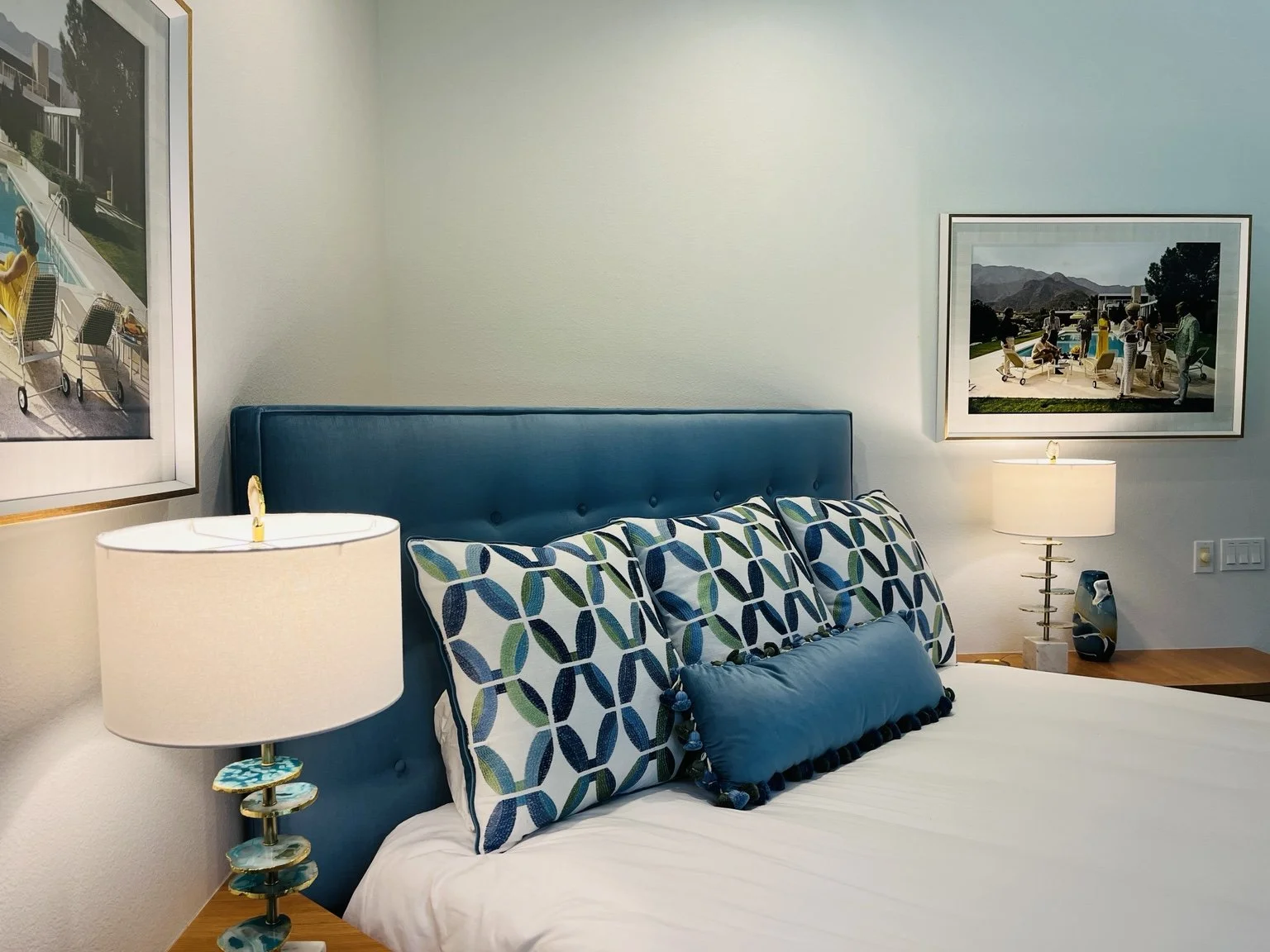 Krista’s bed with a blue upholstered headboard, coordinated patterned pillows, and a blue bolster.