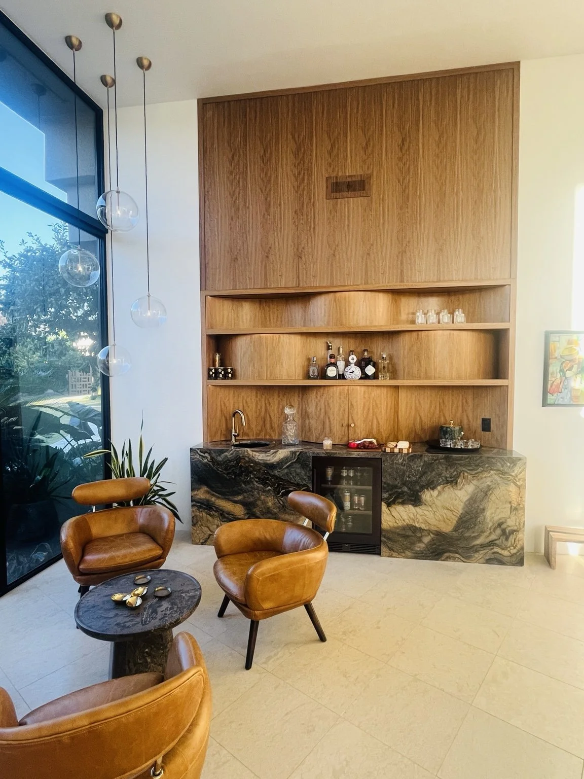 Completed residential wet bar with warm wood cabinetry, open shelving, and richly veined stone.