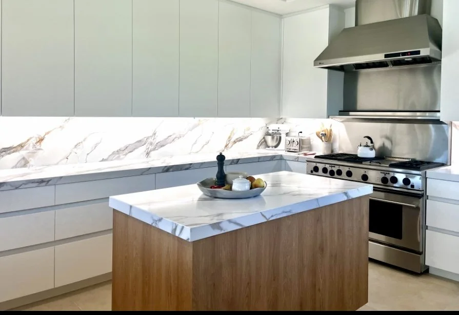 Modern kitchen with white cabinets, marble countertops, a wooden kitchen island, stainless steel stove and range hood, and small appliances on the counter.
