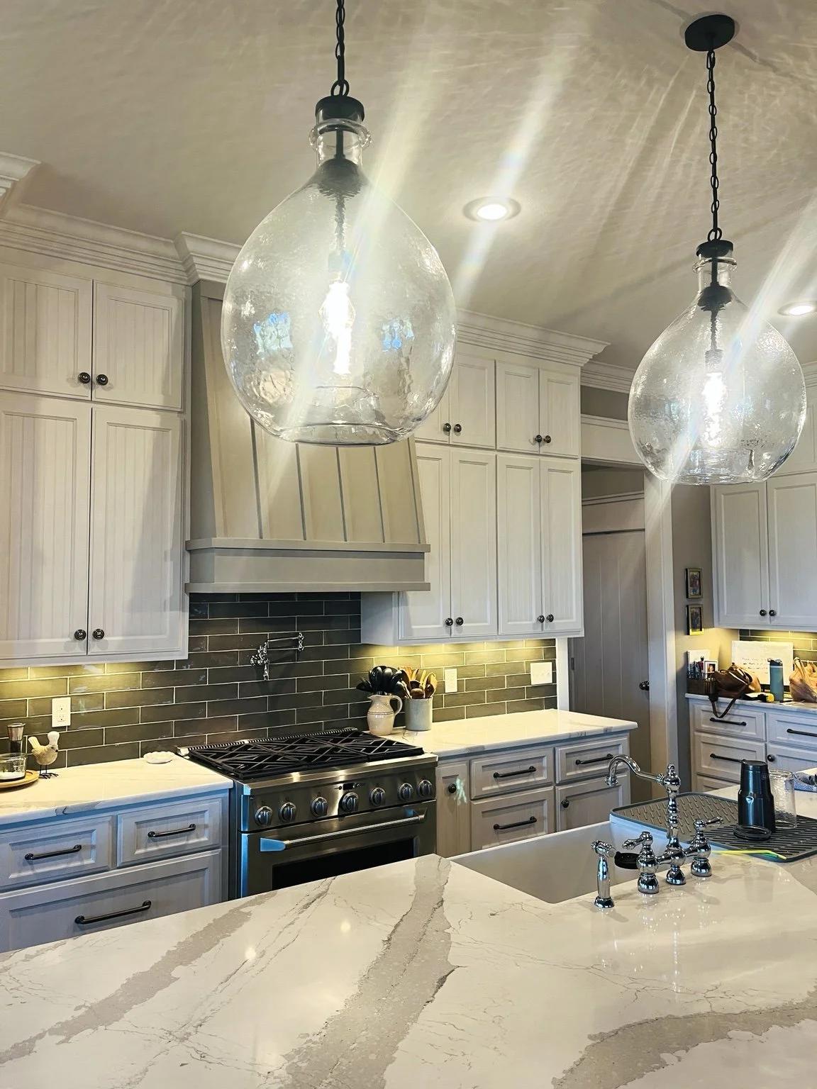 Nicole’s kitchen with light cabinetry, dark tile backsplash, stone countertops, and glass pendant lighting.