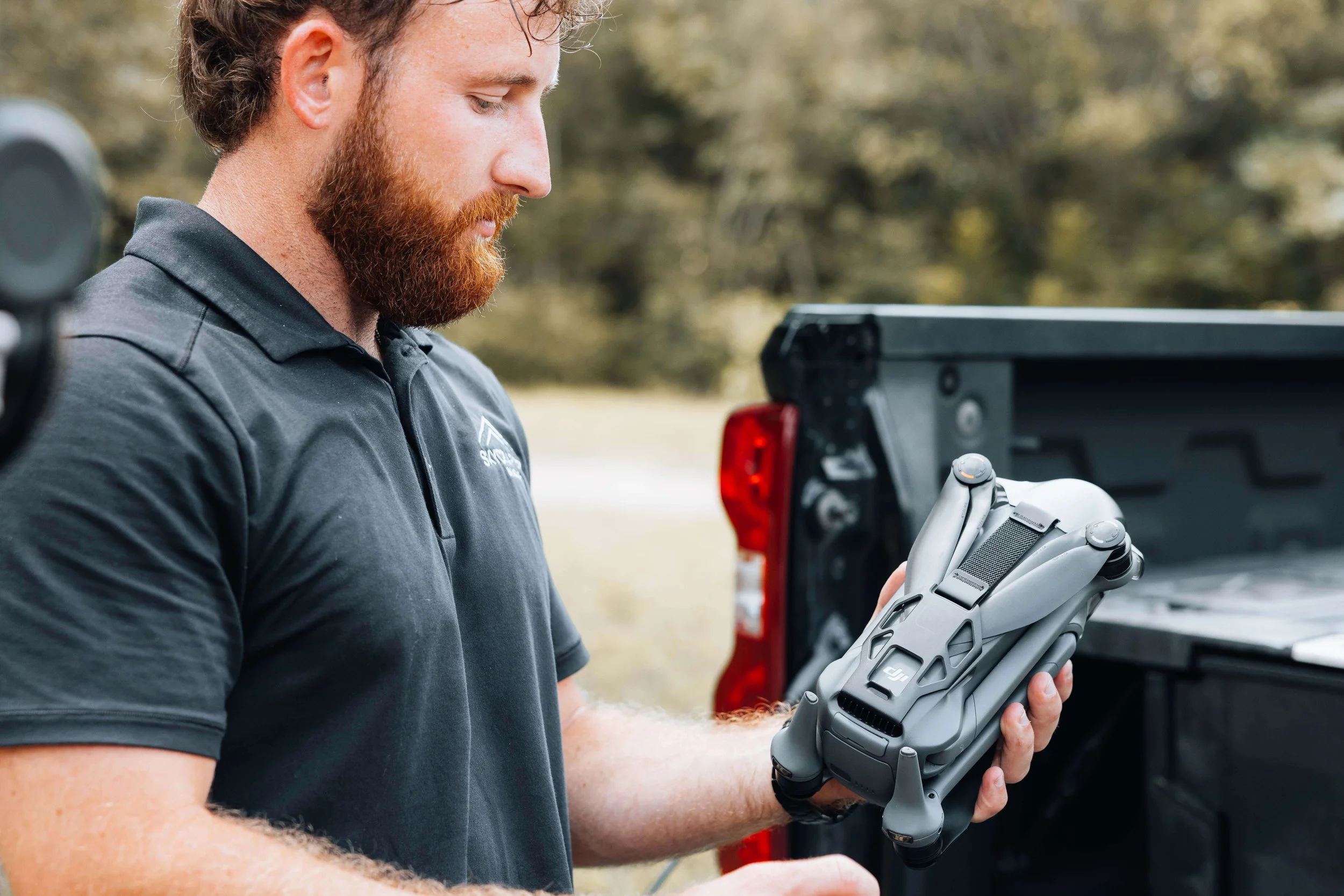 Skycrafted Imaging_Real Estate Media Production_Central & Southeast Texas_A man with a red beard and curly hair looking at a drone controller in his hands, standing outdoors near a pickup truck.