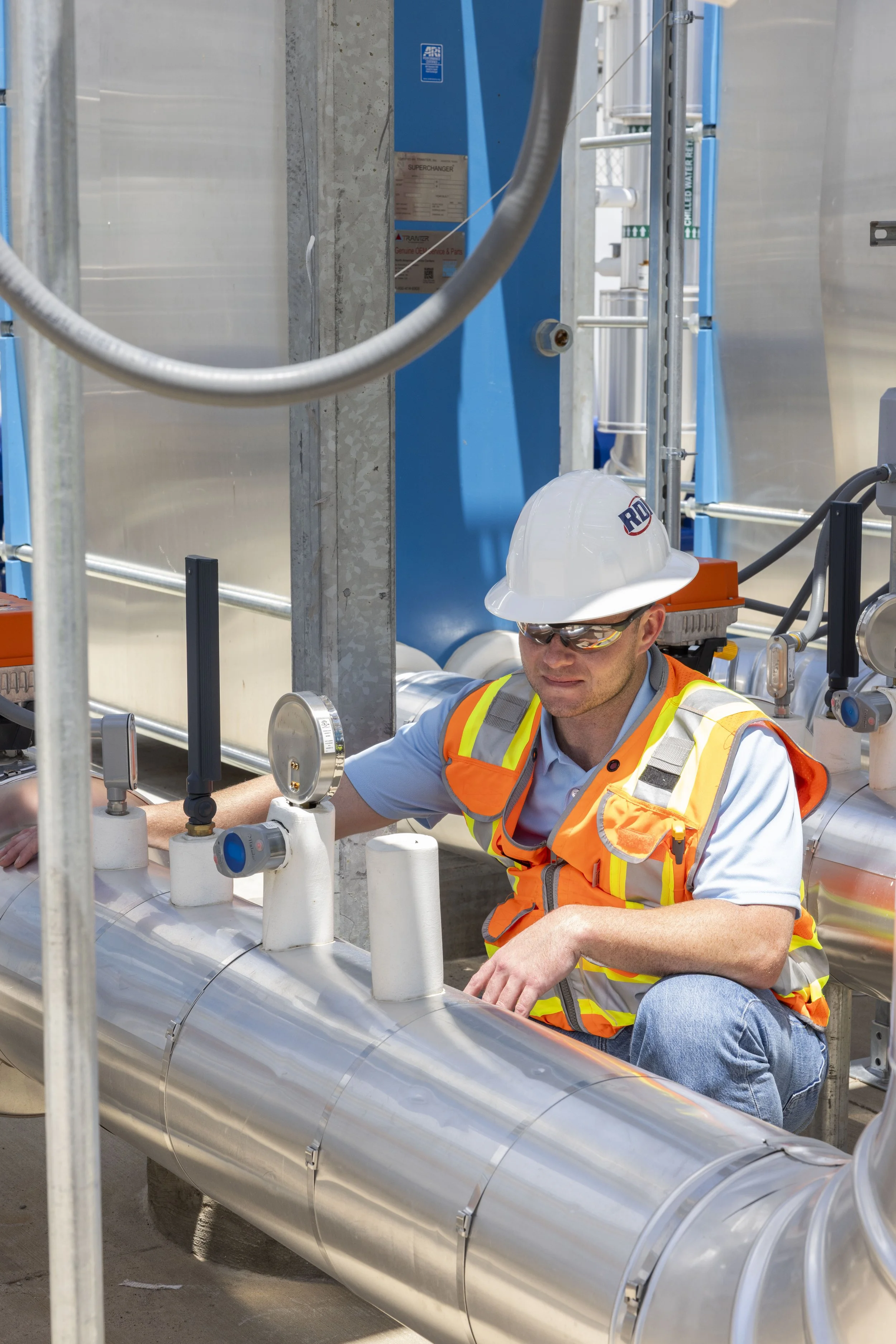 Skycrafted Imaging_Real Estate Media Production_Central & Southeast Texas_A worker wearing a white hard hat and safety glasses is working with industrial pipes and valves at an industrial site.