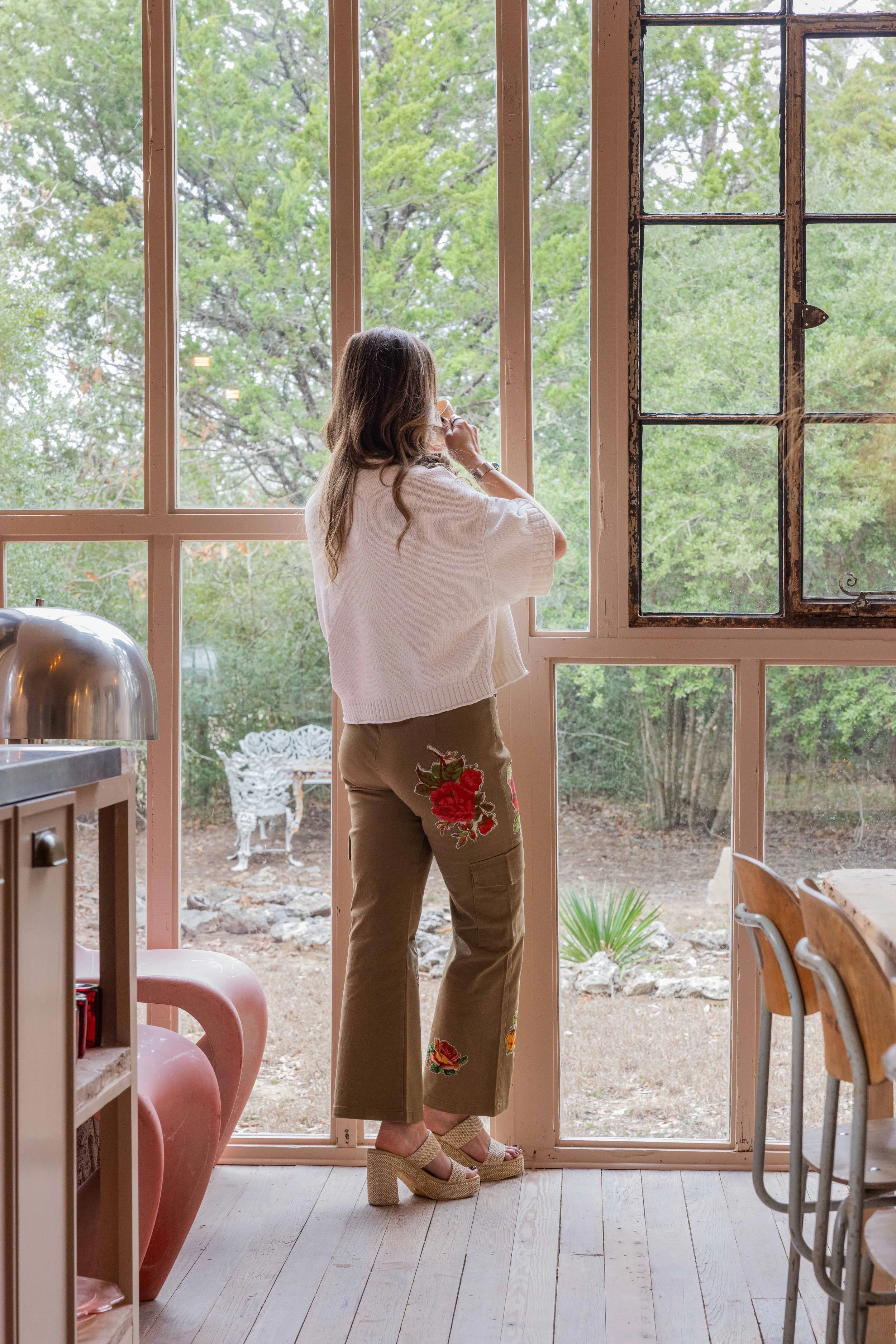Skycrafted Imaging_Real Estate Media Production_Central & Southeast Texas_A woman with long hair wearing a white sweater and tan embroidered pants and platform sandals stands.