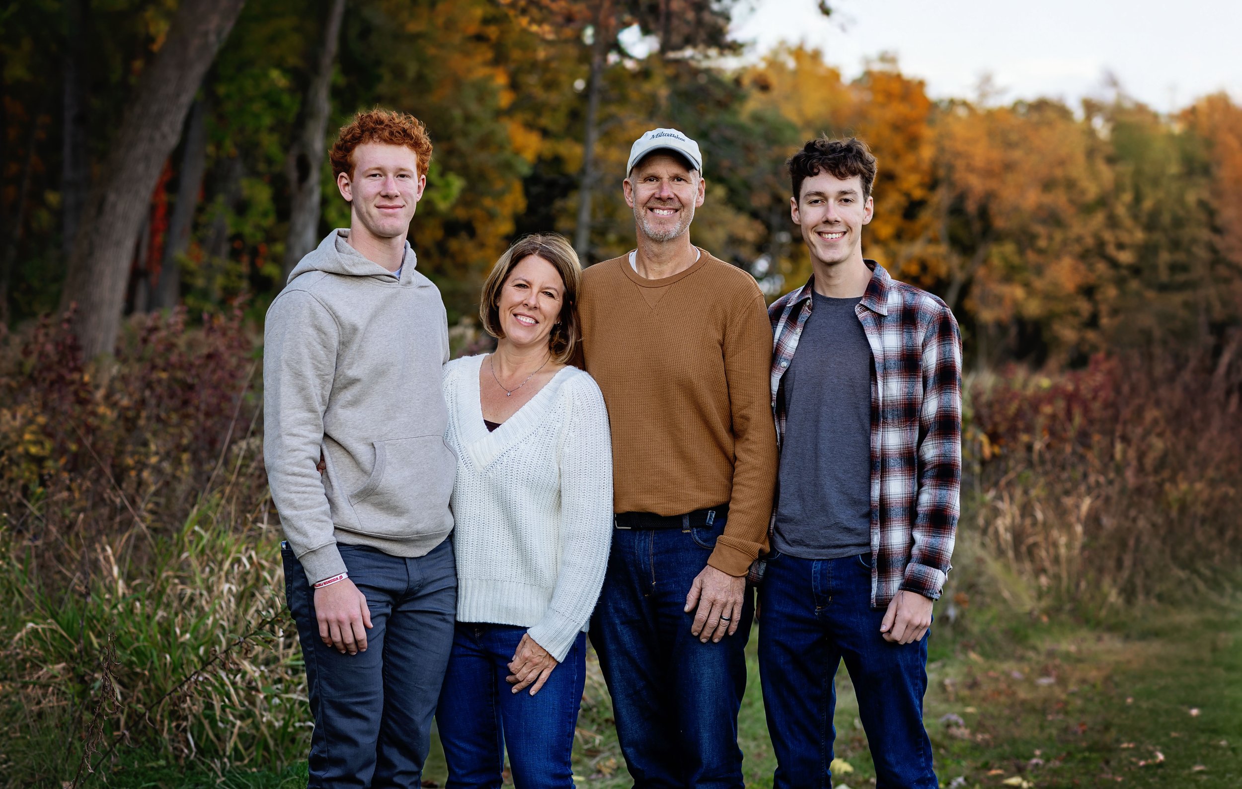 Family of five standing outdoors in fall foliage, smiling at the camera.