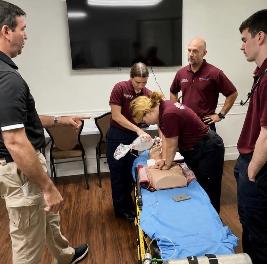 Medical training simulation with four people practicing CPR on a baby mannequin, with others observing.