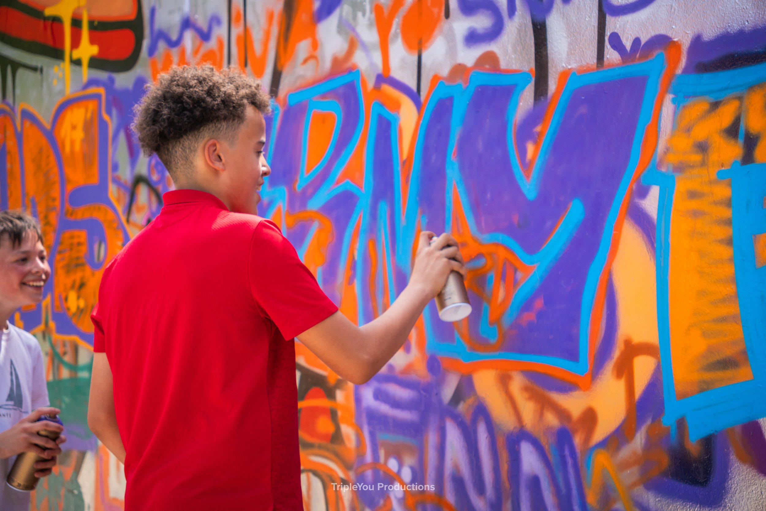 Een jongen die met graffiti kunst maakt op een kleurrijke muur.