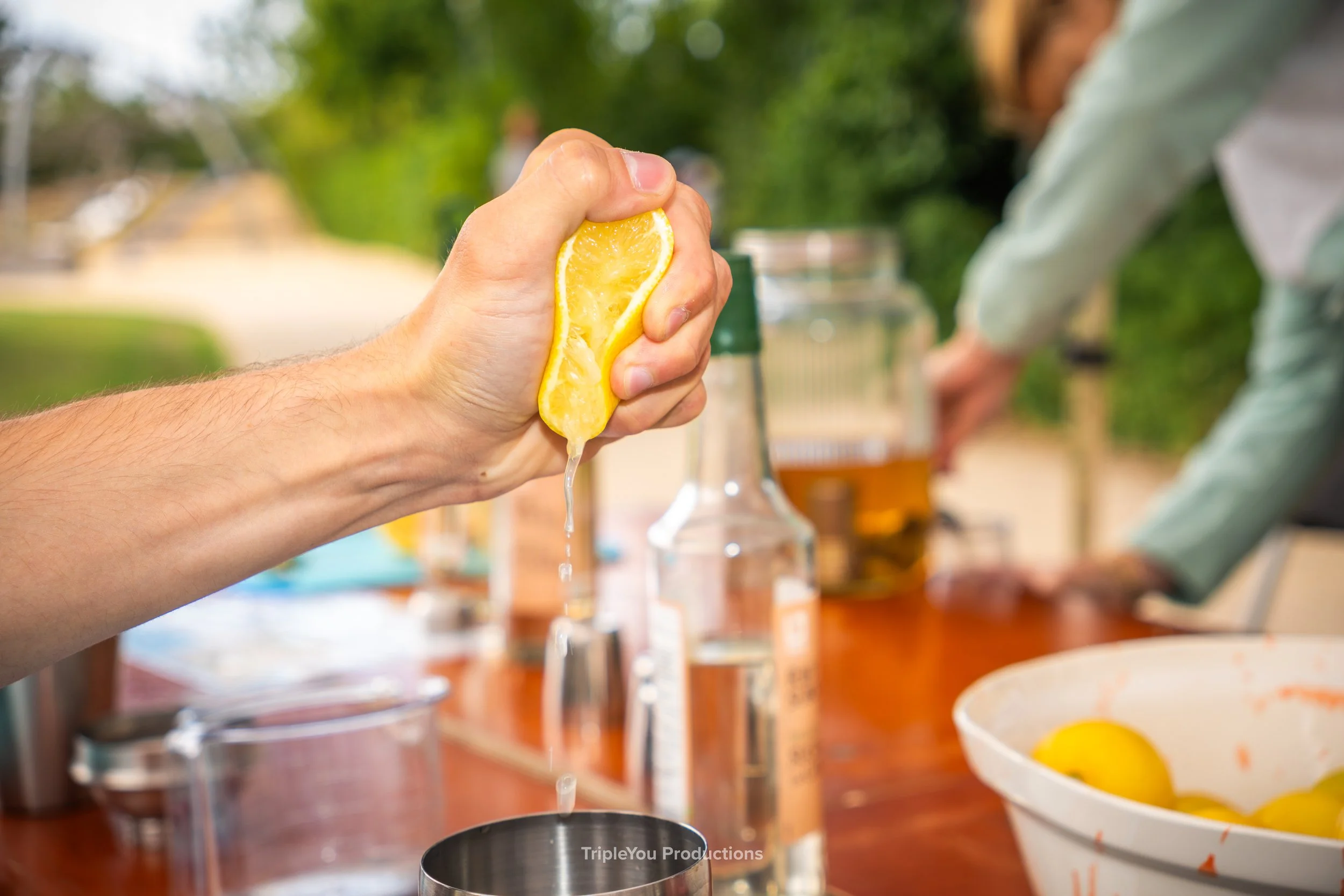 Close-up shot van een hand die een citroen uitknijpt in een metalen kom op een tafel buiten.