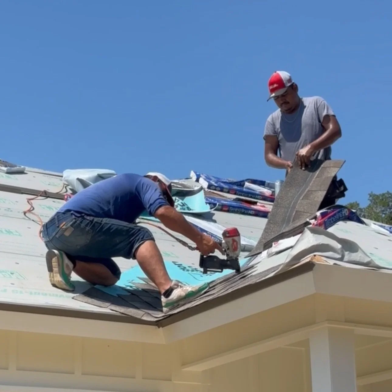 Two men working on a roof, installing or repairing shingles under a blue sky in Victoria, Texas.
