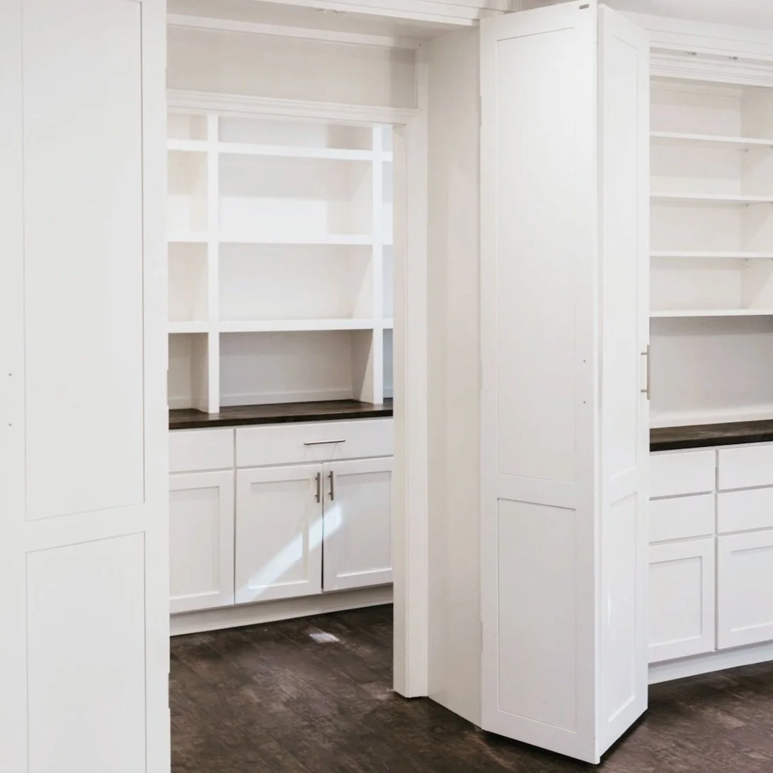 Newly remodeled dining rom with empty white kitchen cabinets with open shelving, drawers, and dark wood flooring.