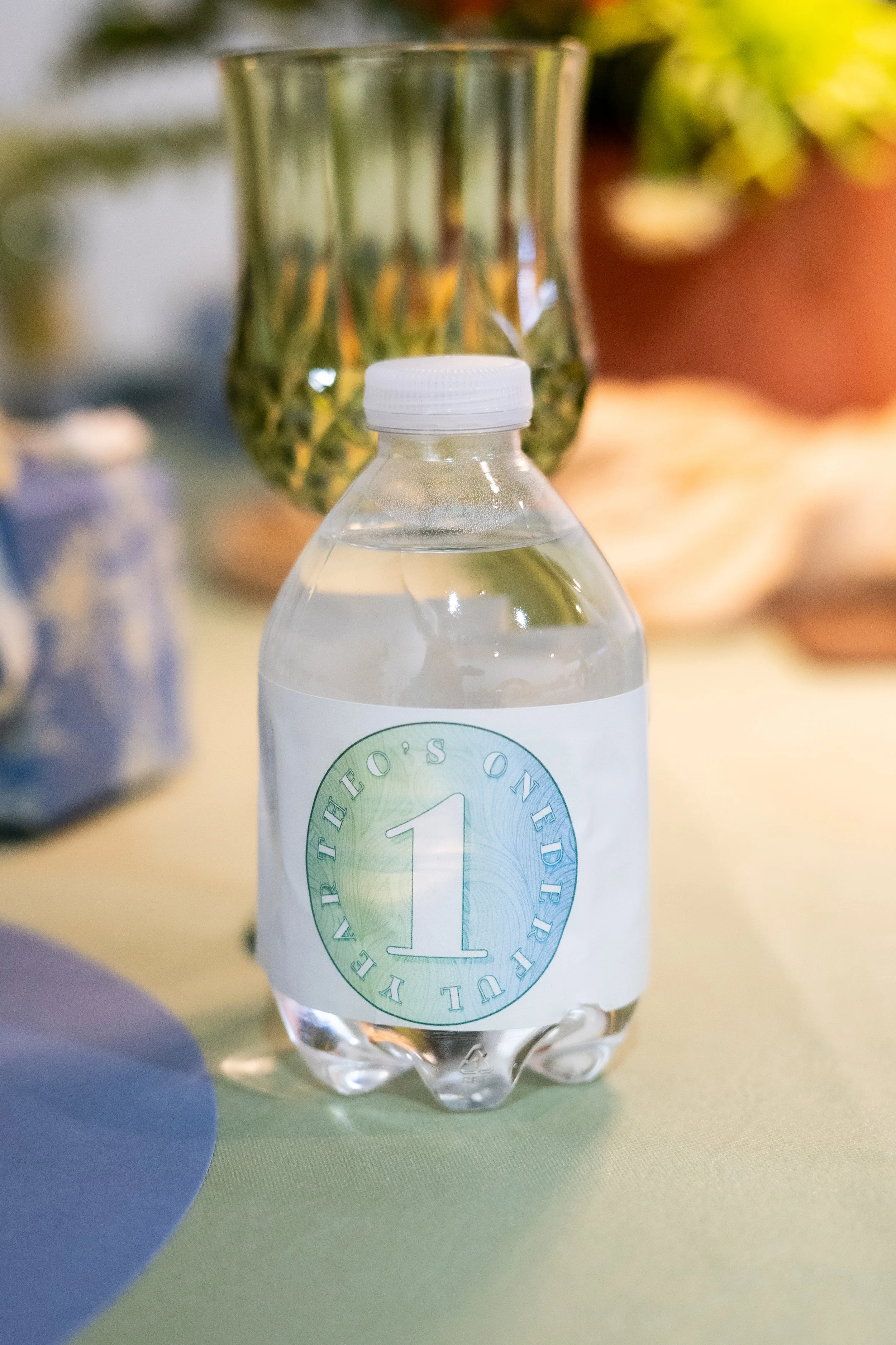 Close-up of a plastic water bottle with a white cap, placed on a multicolored surface with blurred objects in the background.