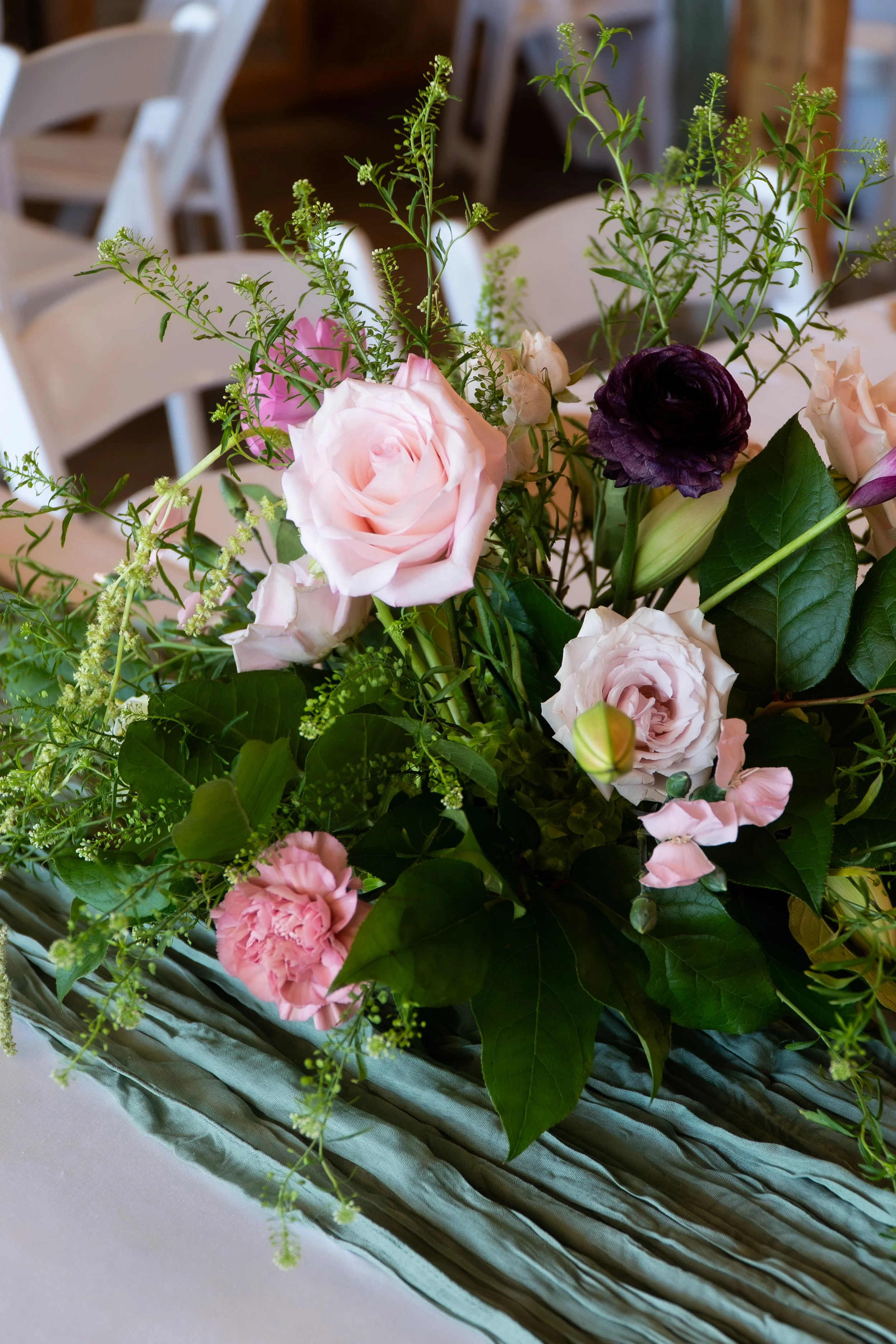 Pink and purple flowers with green foliage in a floral arrangement on a table.