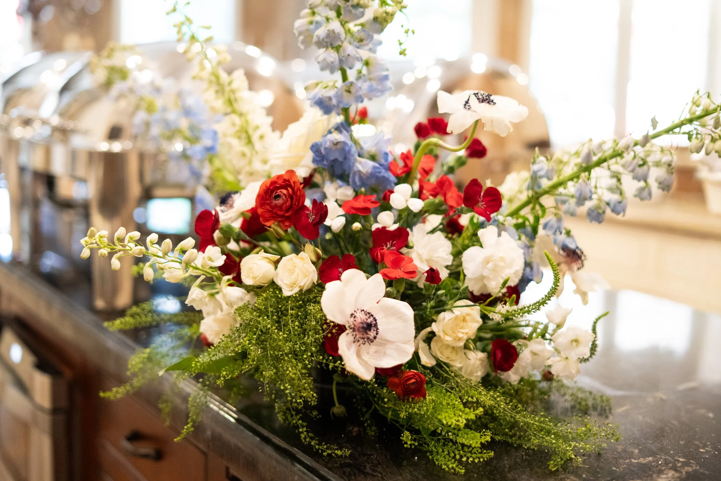 A colorful floral arrangement featuring white, red, blue, and purple flowers placed on a counter in a well-lit indoor setting.