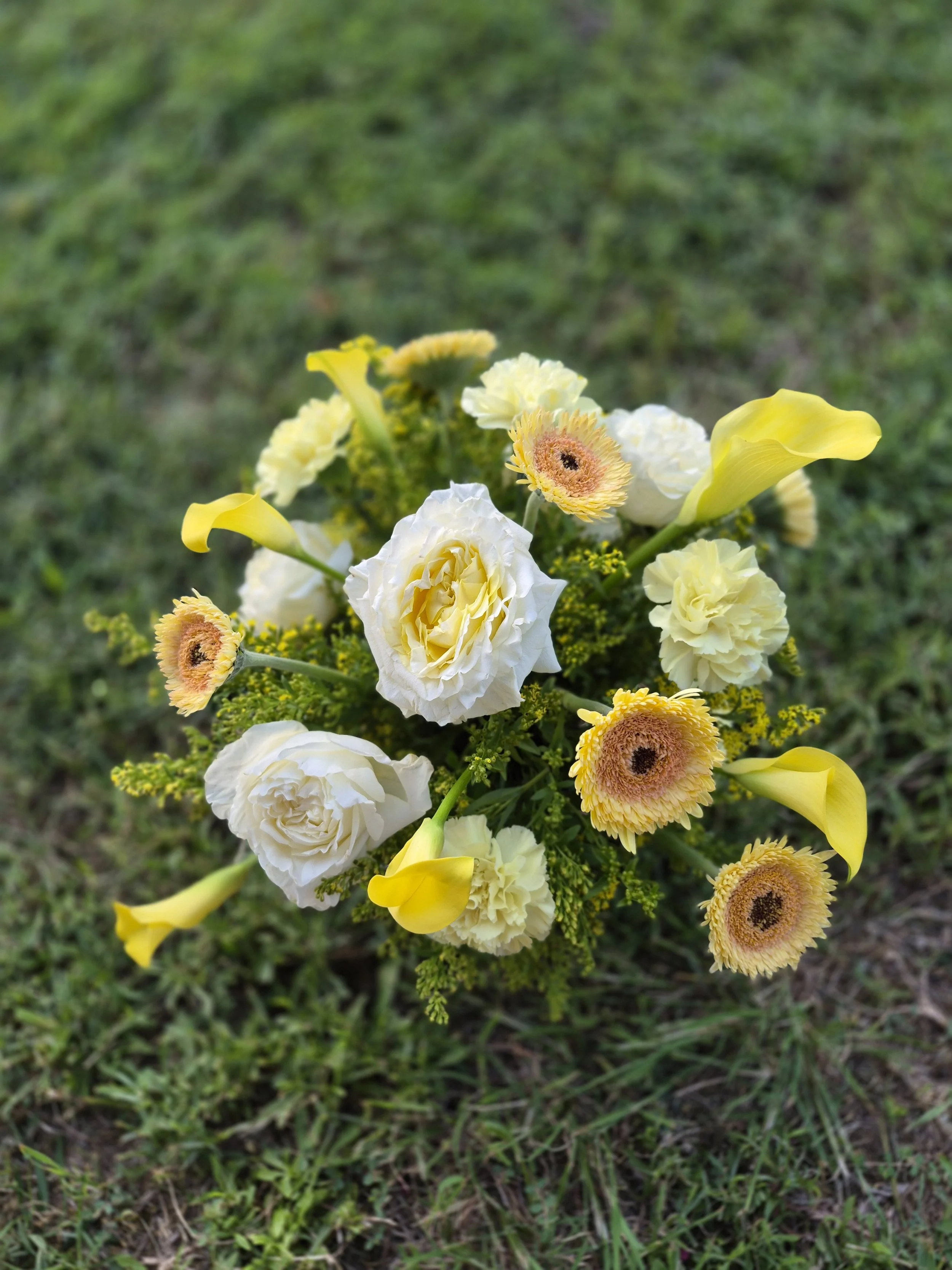 A bouquet of yellow and white flowers on grass ground.
