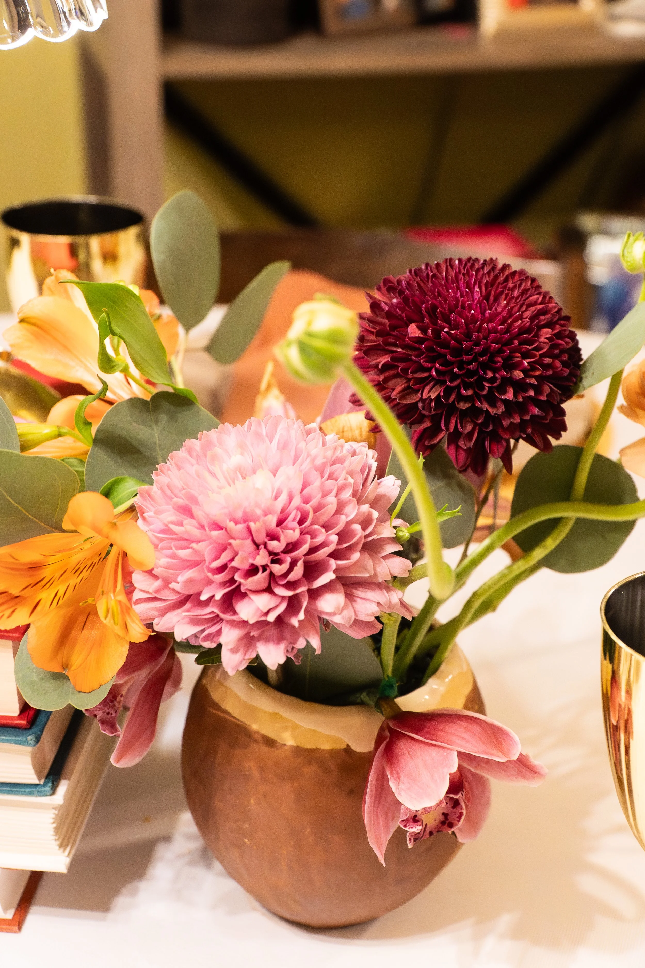 A floral arrangement with pink dahlias, orange lilies, and purple flowers in a brown vase on a table.