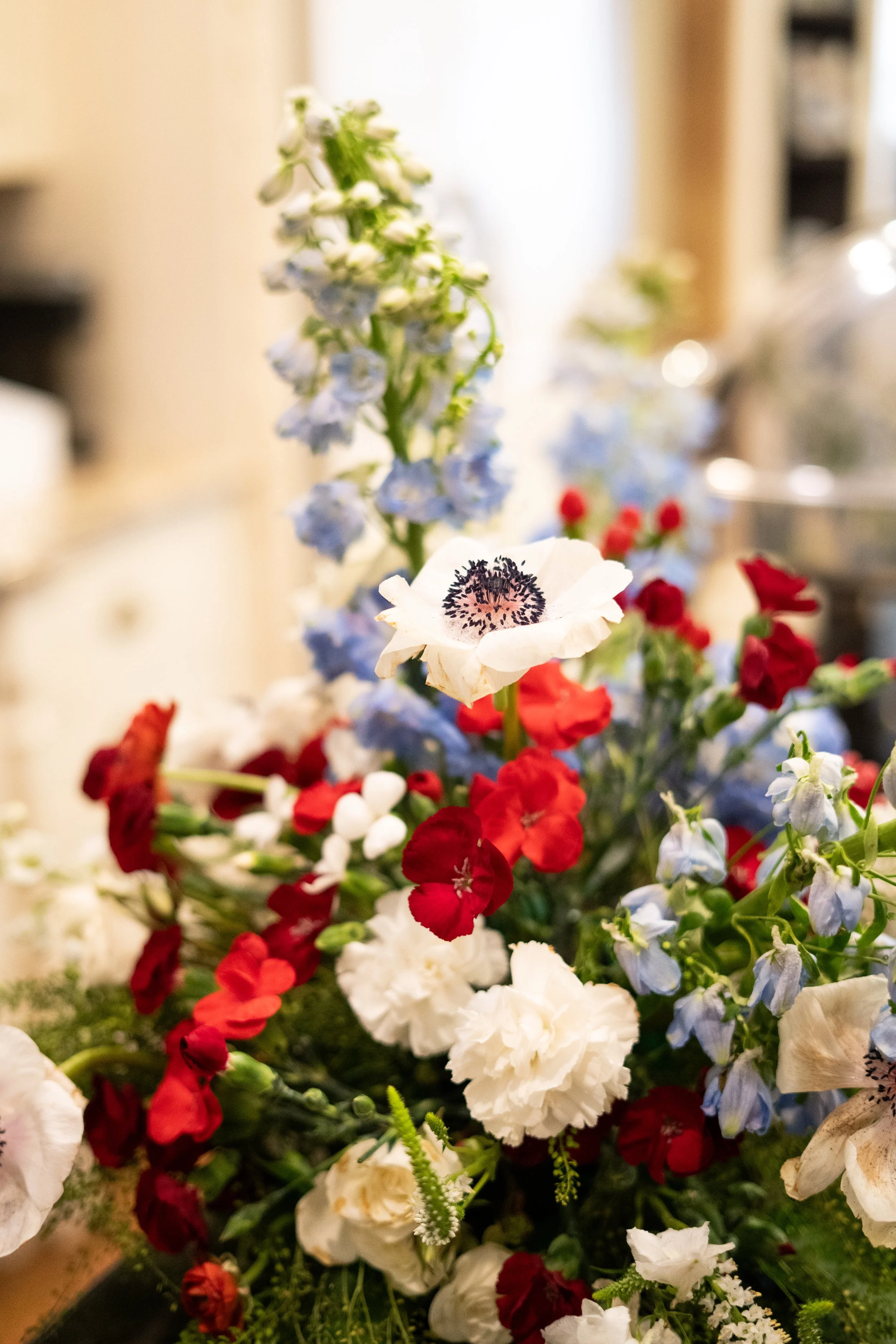 A bouquet of various flowers, including white, red, and light blue blooms, with soft indoor lighting in the background.
