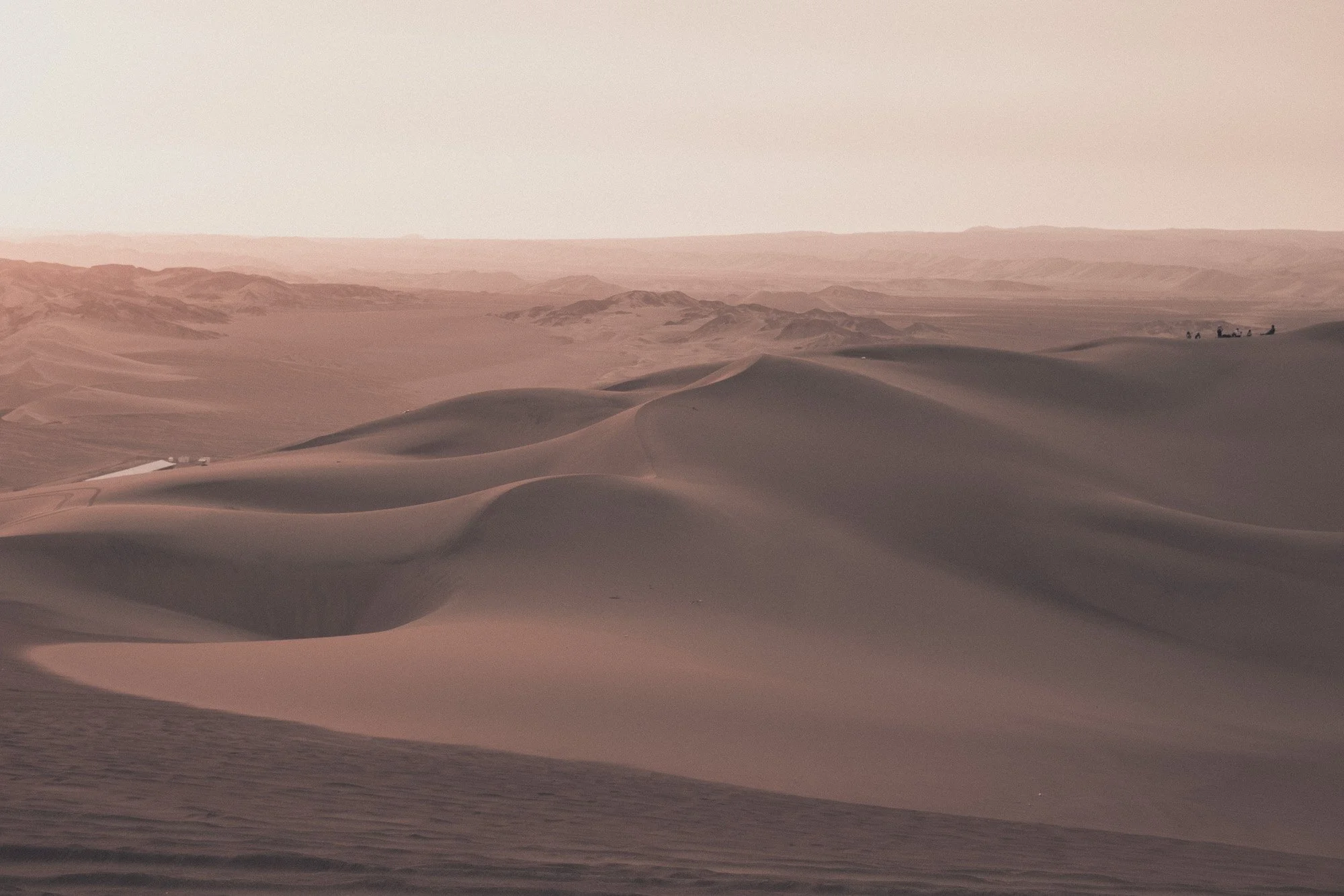 Sand dunes in a desert landscape with a distant caravan of camels and people.