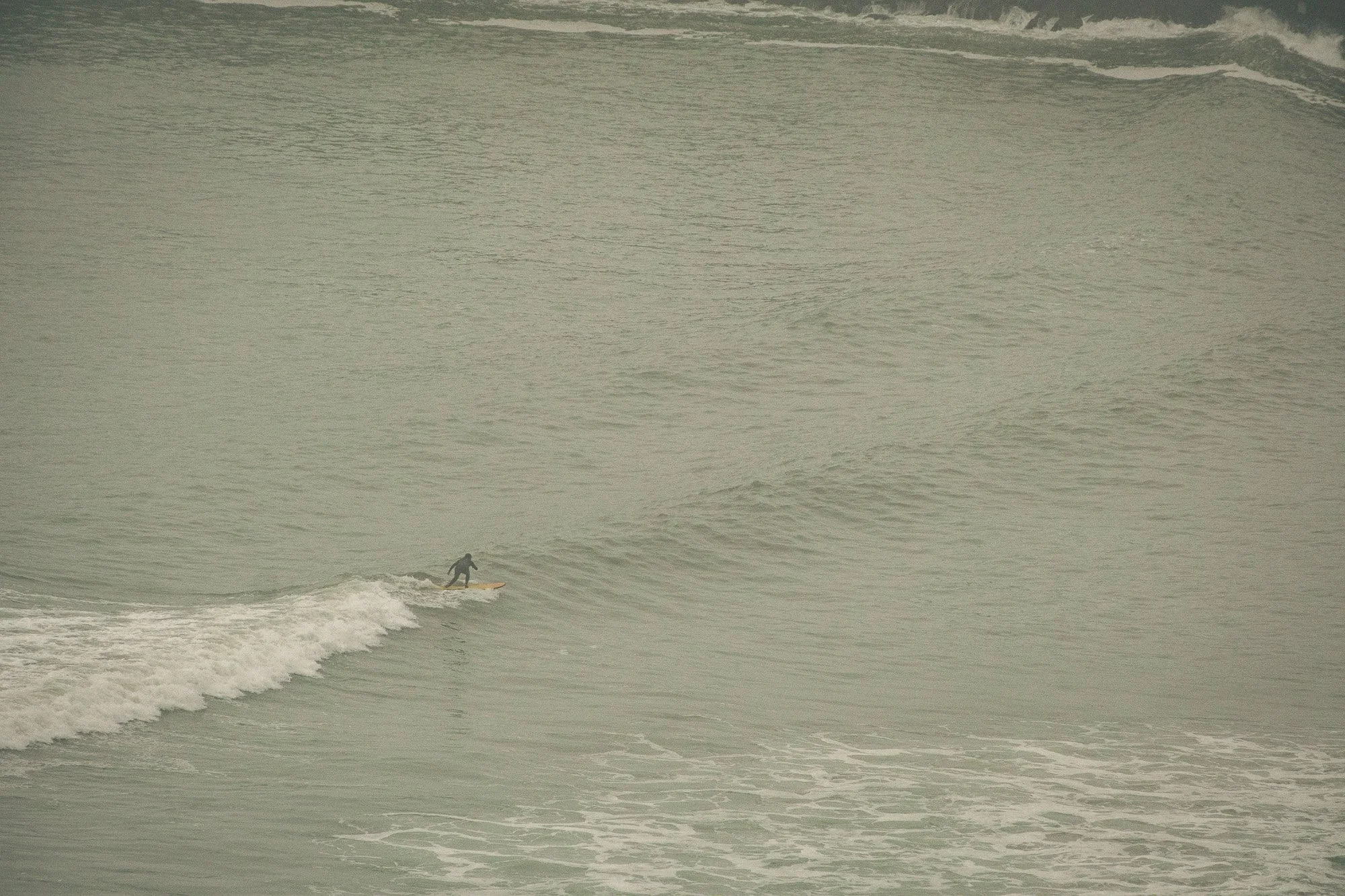 A person surfing on a wave in the ocean during overcast weather.