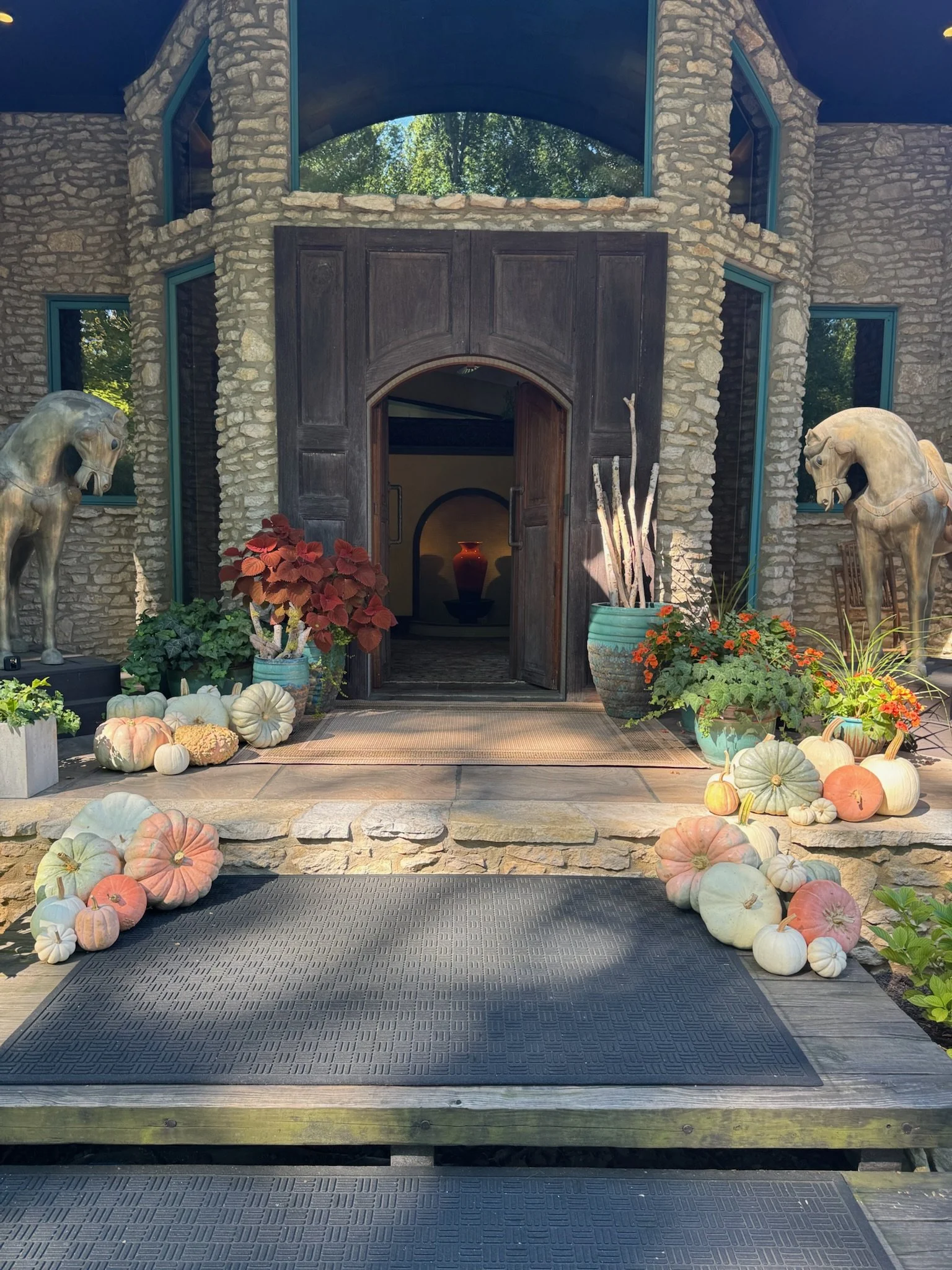 Decorative pumpkins in pastel colors and orange are arranged on hay bales in front of a white barn under a full moon at night.
