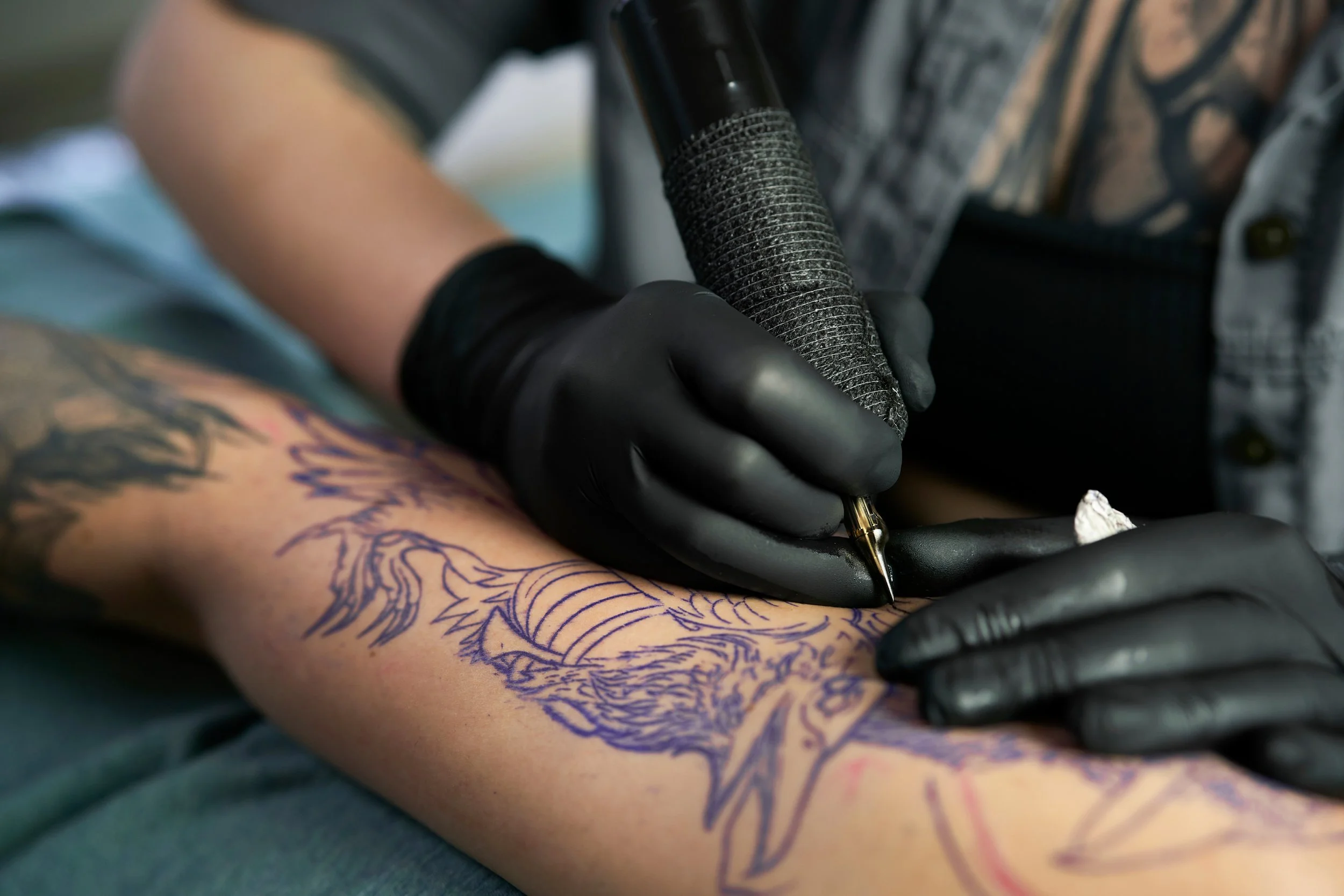 A person with tattoos getting a tattoo of a lion's face on their forearm, using a tattoo machine.
