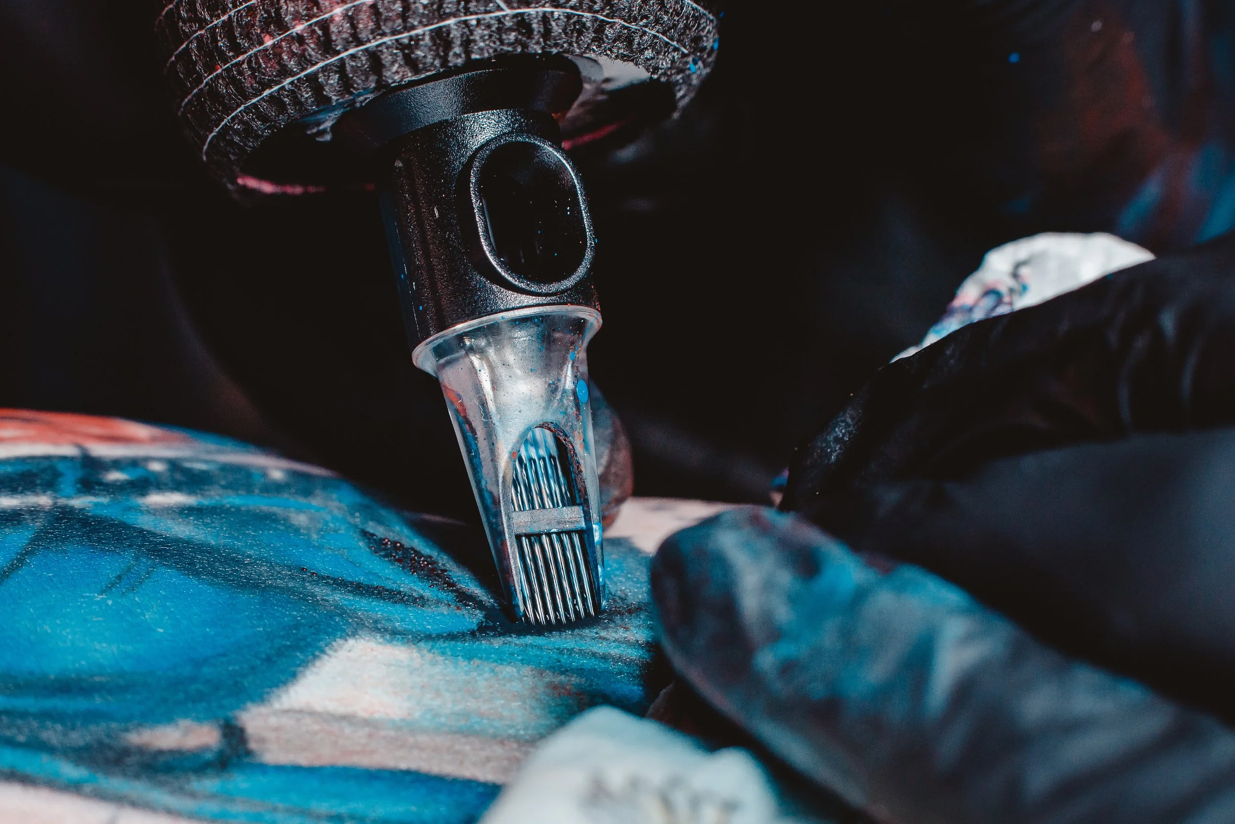Close-up of a tattoo machine and a gloved hand during tattooing.