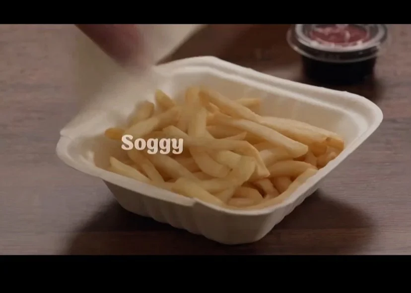 A container of French fries with the word "Soggy" overlayed on top, and a small cup of dipping sauce in the background.