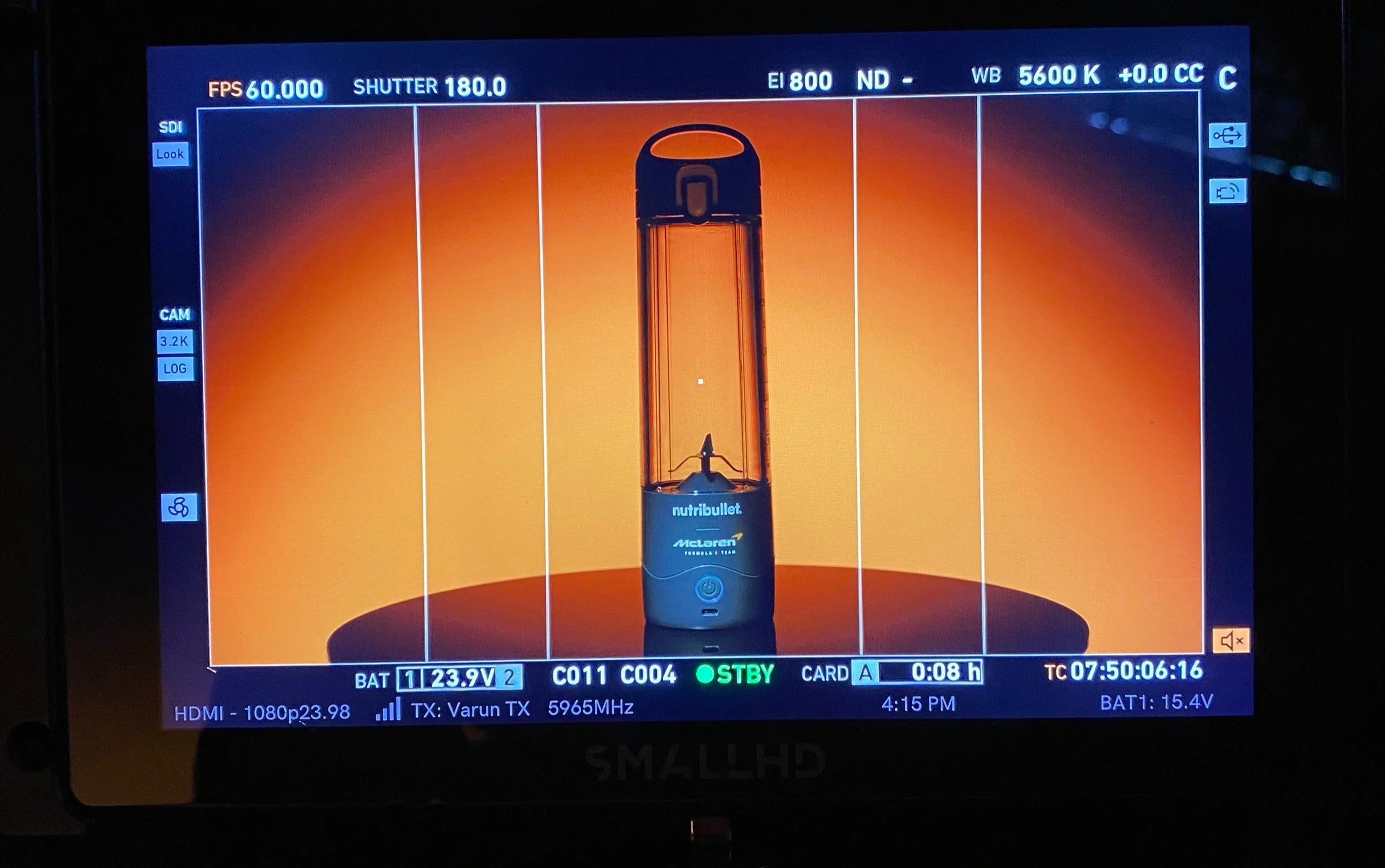 Camera viewfinder screen displaying a close-up of a NutriBullet blender with a black base and an orange blending jar, branded with McLaren, set against a gradient orange background.