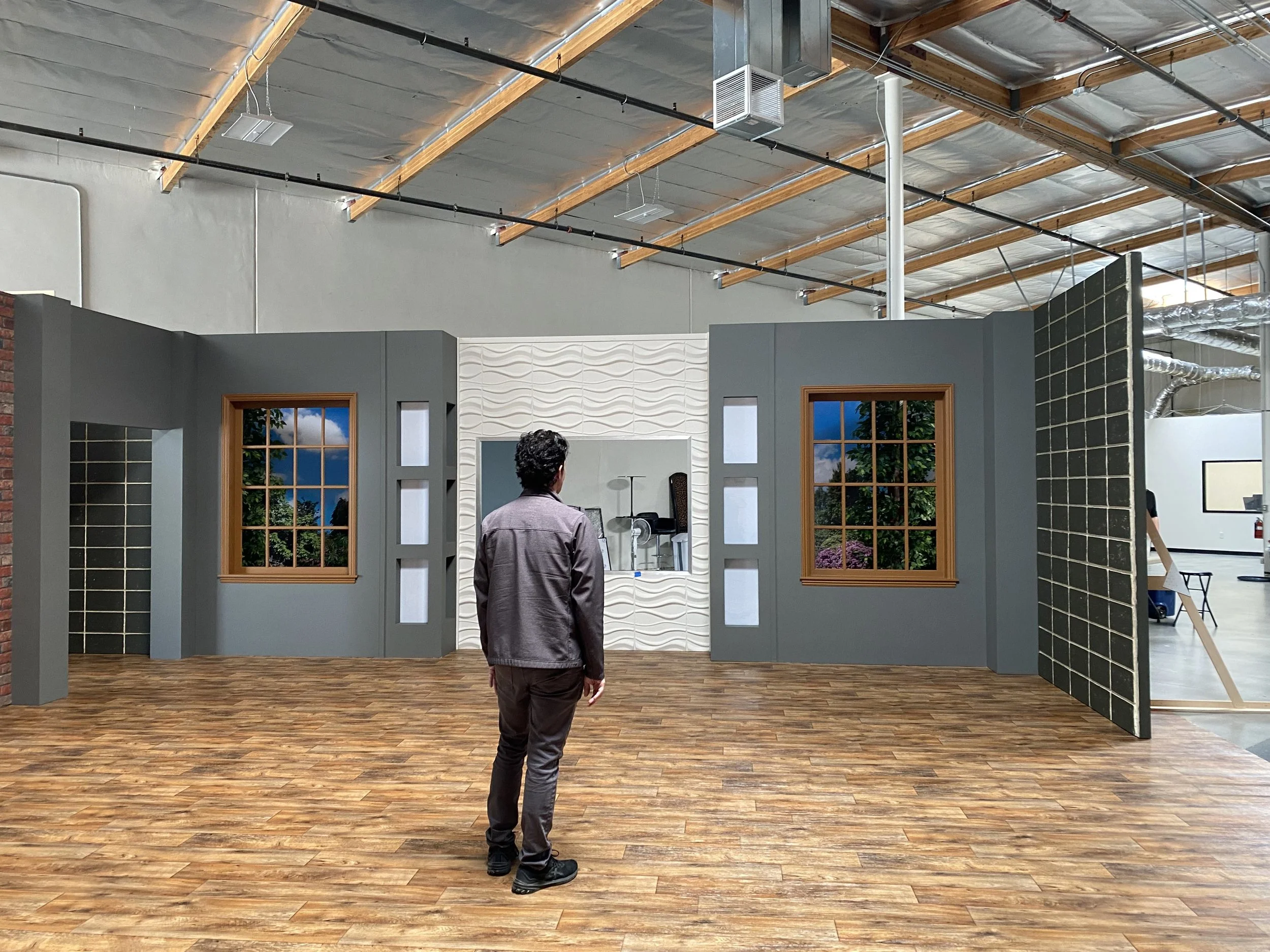 Person standing in a room with decorative walls, windows, and a patterned background, in an industrial-style space with a raised ceiling and exposed ductwork.