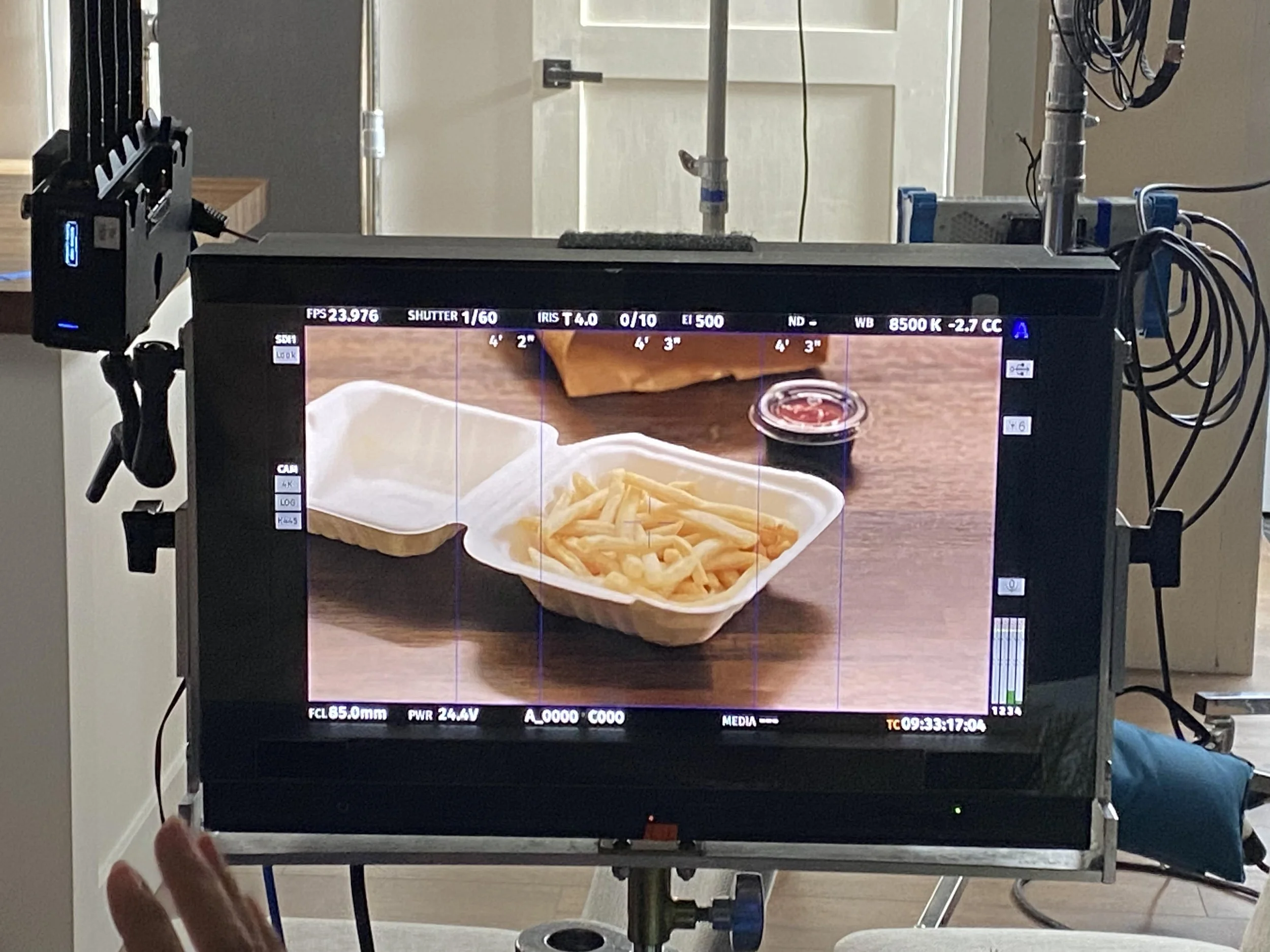 Video monitor displaying a food tray with French fries, soy sauce, and a water bottle on a wooden table.